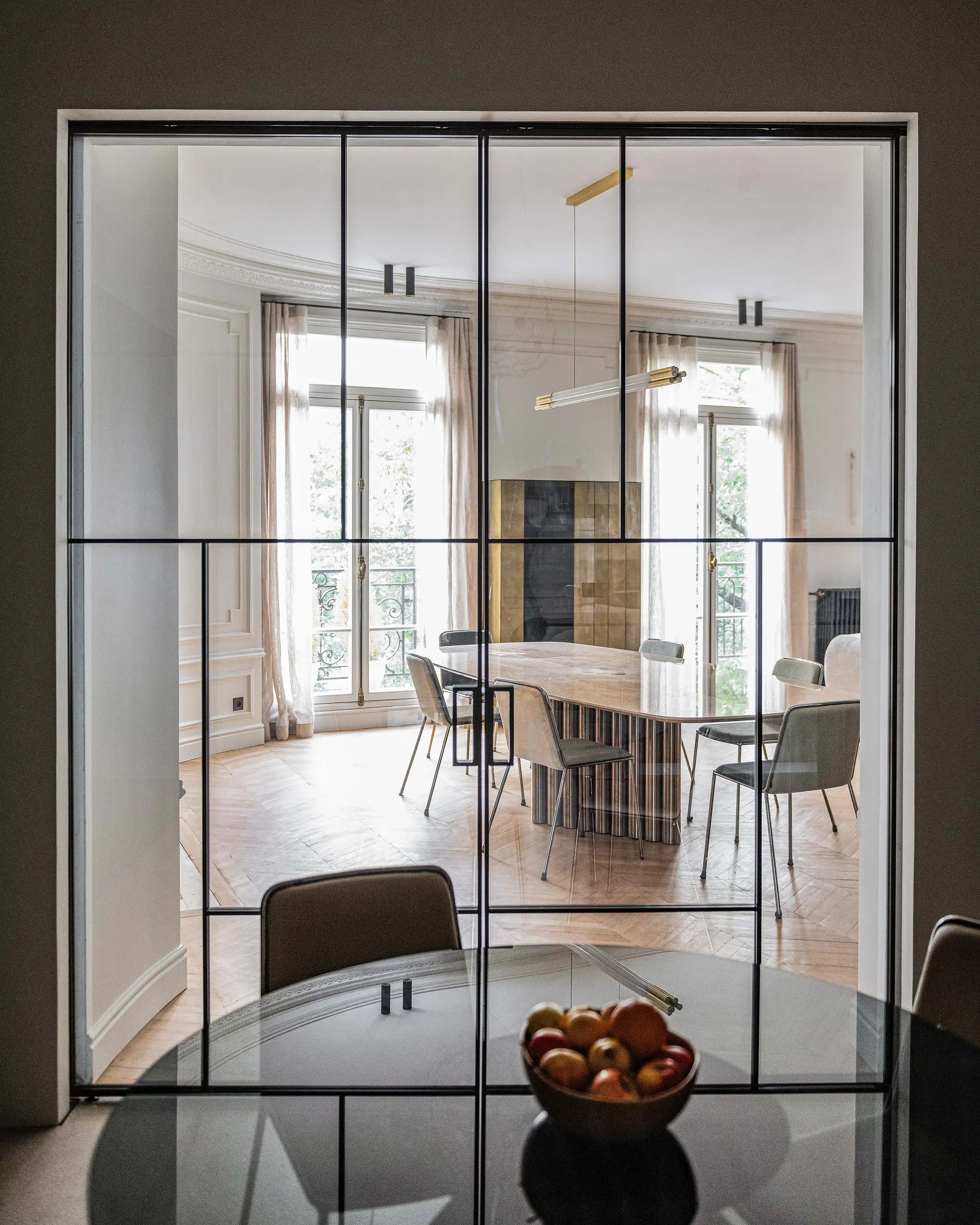 Grande verrière intérieure à structure fine noire séparant la cuisine de la salle à manger dans un appartement parisien rénové.