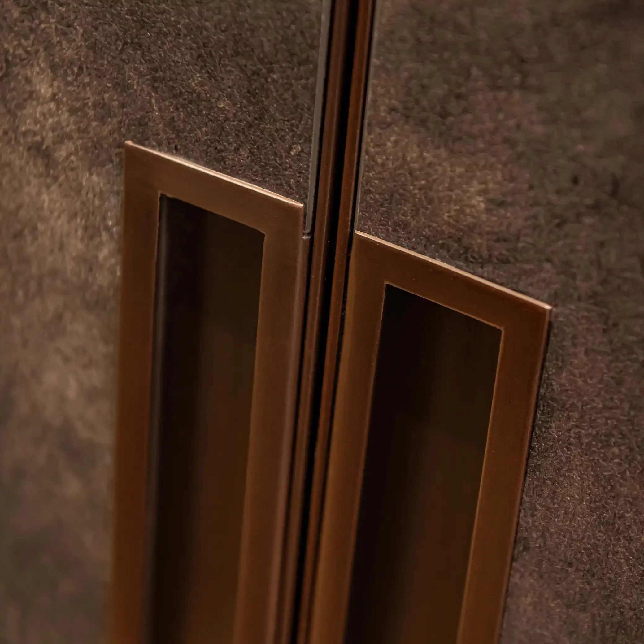 Détail de poignées de porte minimalistes en bronze brossé sur un  dressing en placage façon cuir.