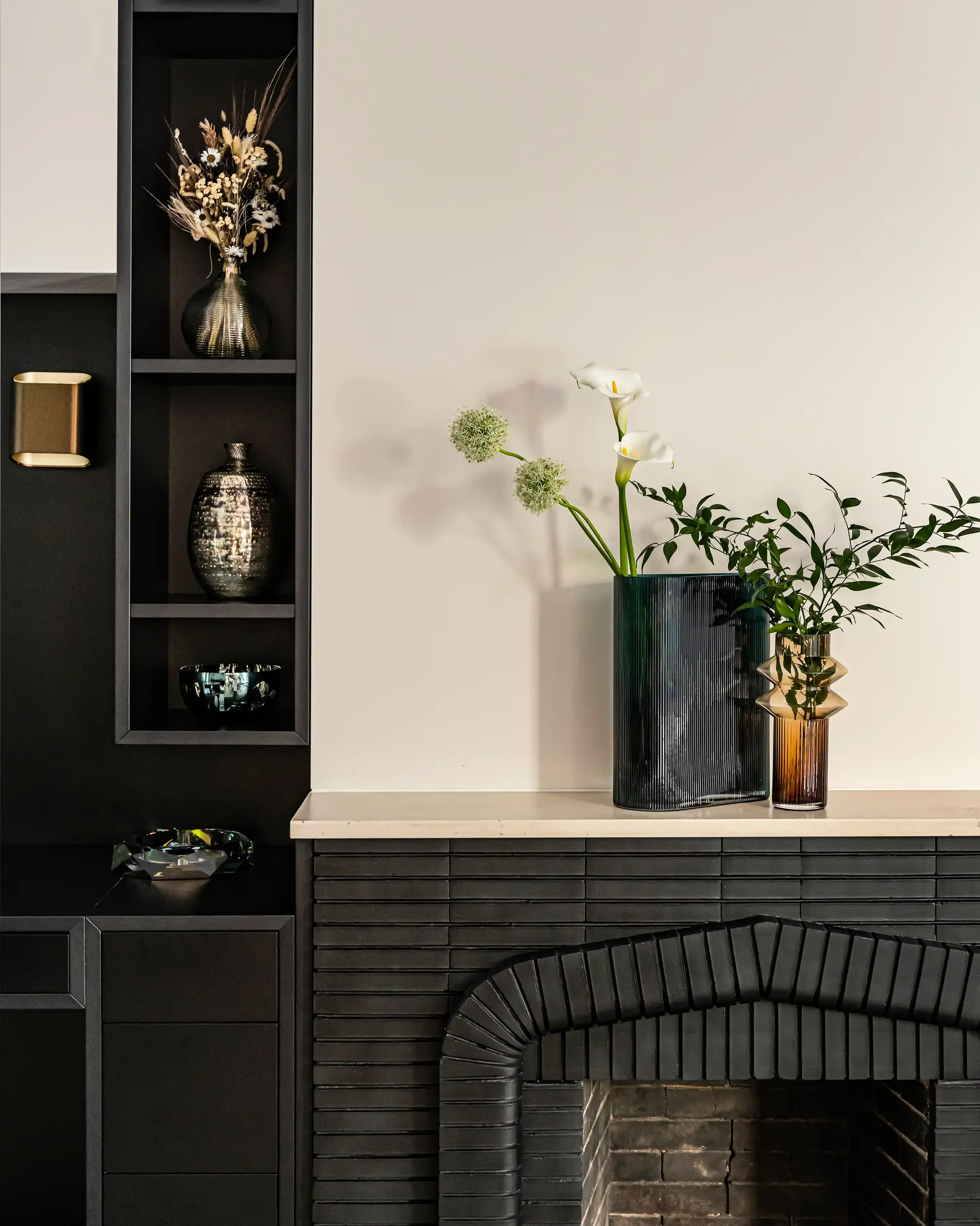 Détail d'architecture d'intérieur : cheminée moderne habillée de briques noires et étagères sur-mesure.