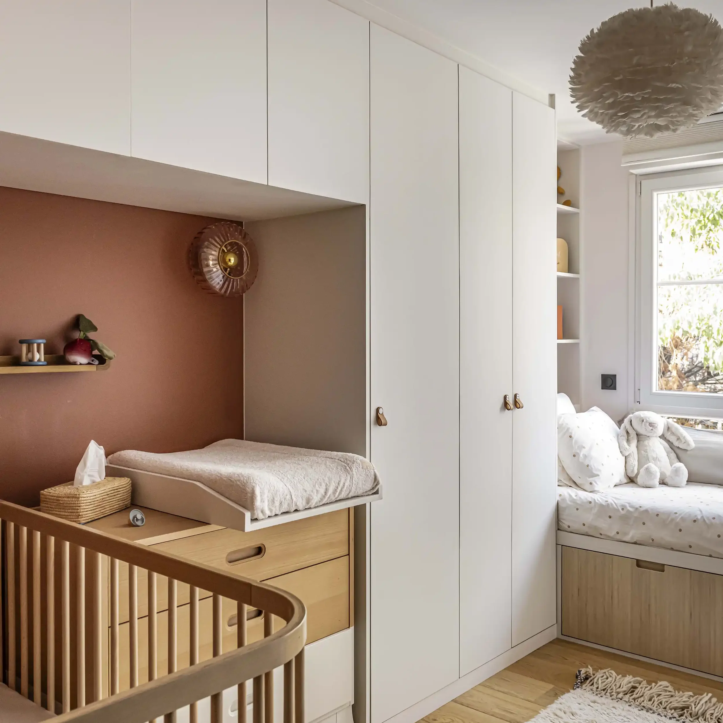 Aménagement de chambre bébé avec plan à langer sur mesure intégré dans une niche terracotta et placards blancs.