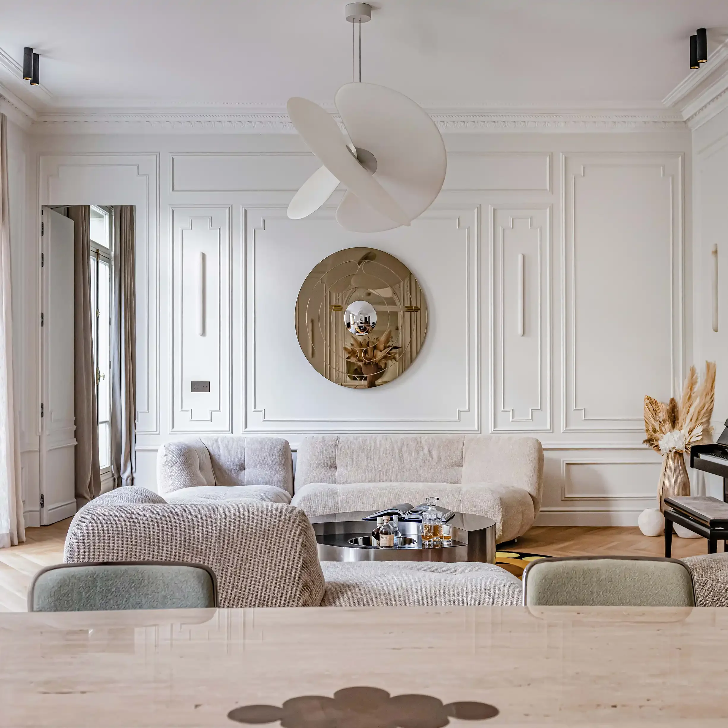 Salon contemporain avec canapé modulable beige, miroir design et grandes moulures murales classiques.