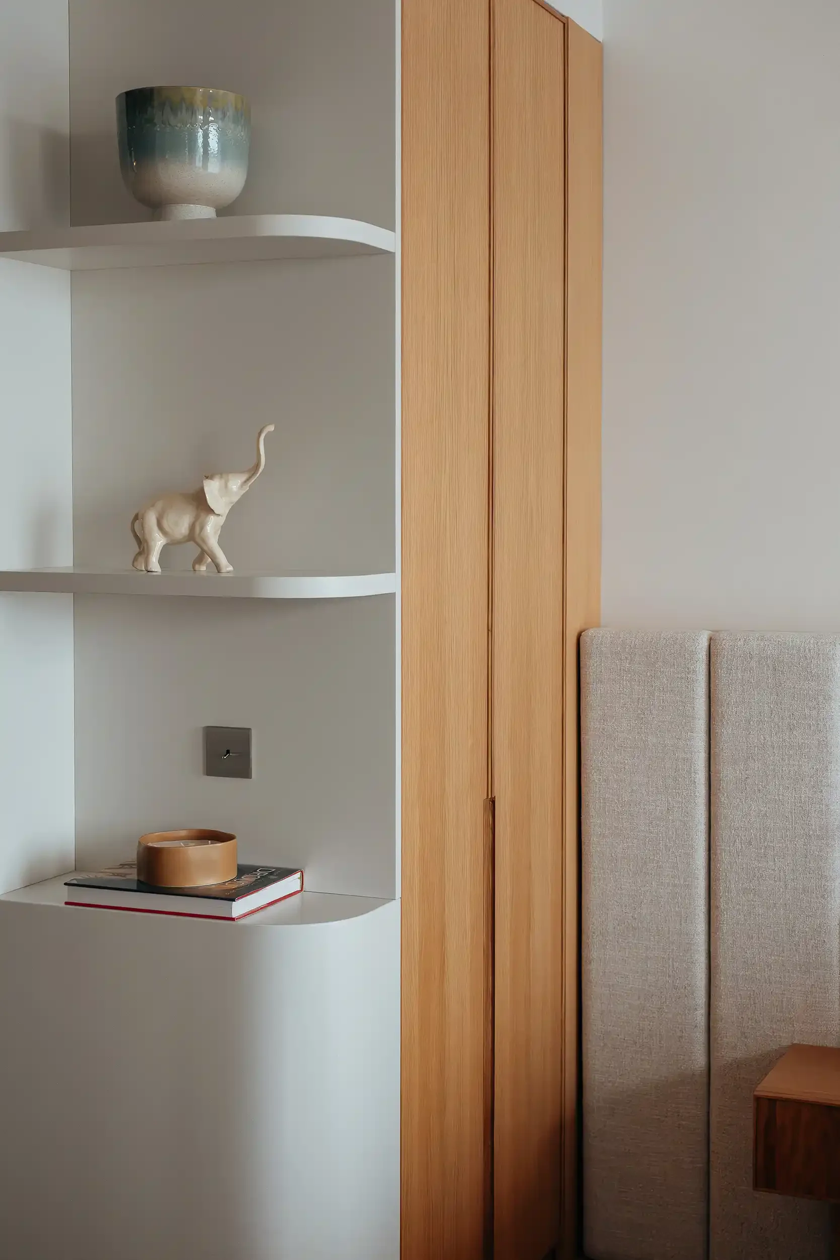 Détail d'une étagère design blanche aux angles arrondis intégrée à un dressing en bois minimaliste.