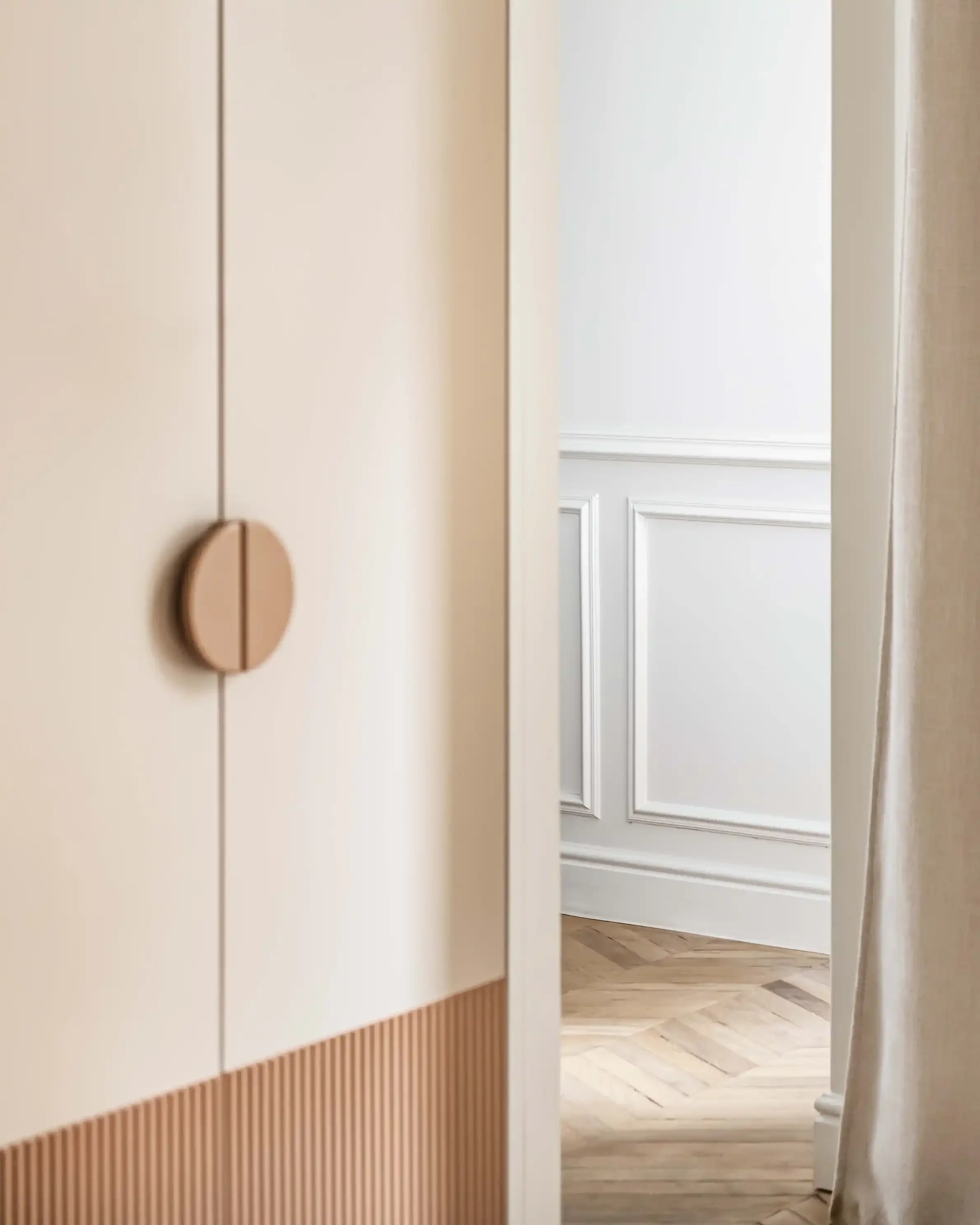 Détail d'un placard de luxe beige avec soubassement cannelé ocre et sol en parquet point de Hongrie.