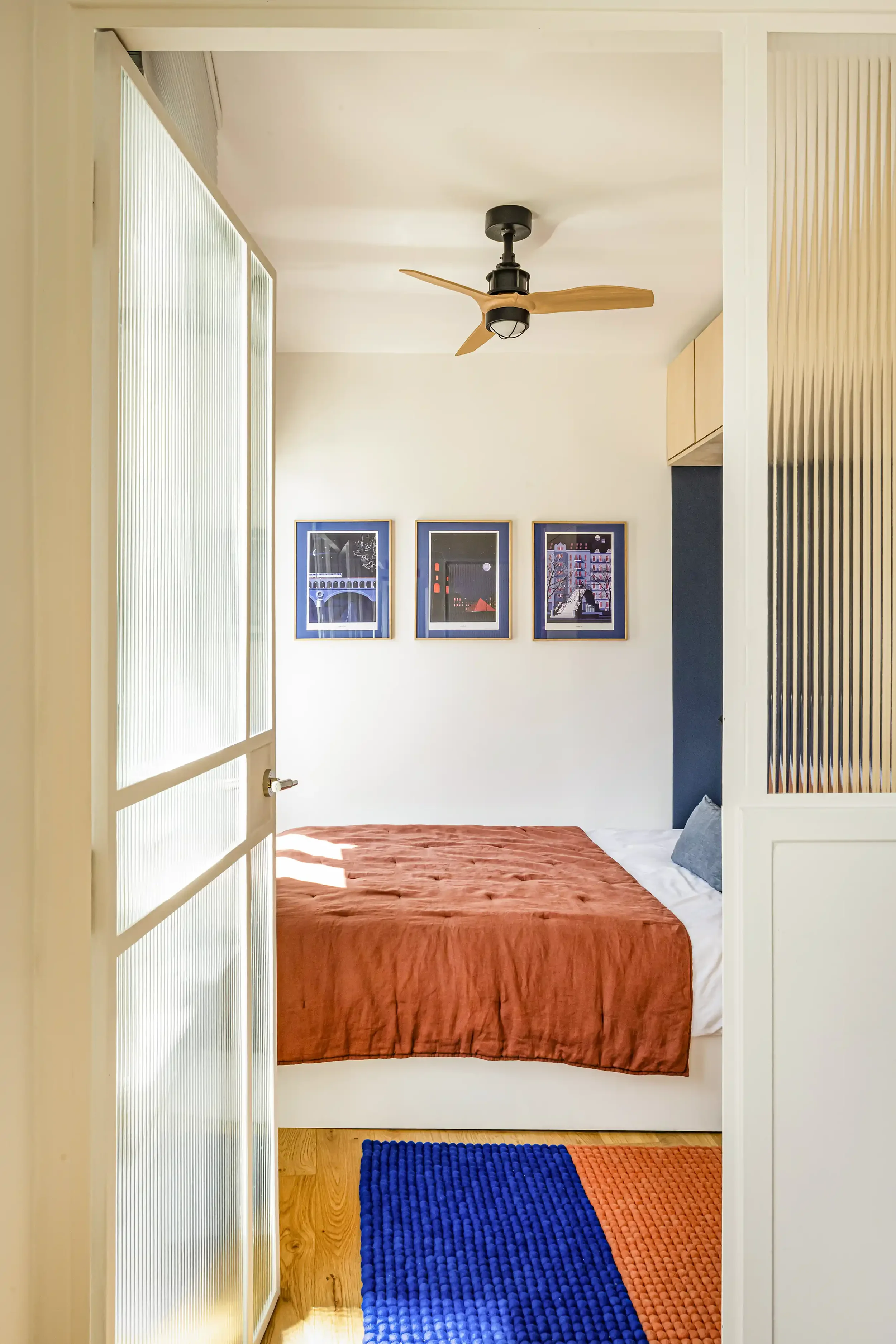 Séparation de chambre en studio avec verrière en verre flûté et cadre en bois pour préserver l'intimité et la lumière.