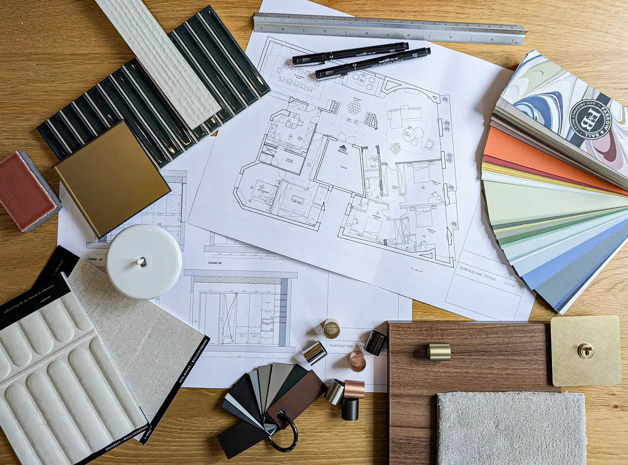 ue de dessus d'un bureau d'architecte avec plans de masse, nuancier Farrow & Ball, échantillons de carrelage, tissus et finitions en laiton.