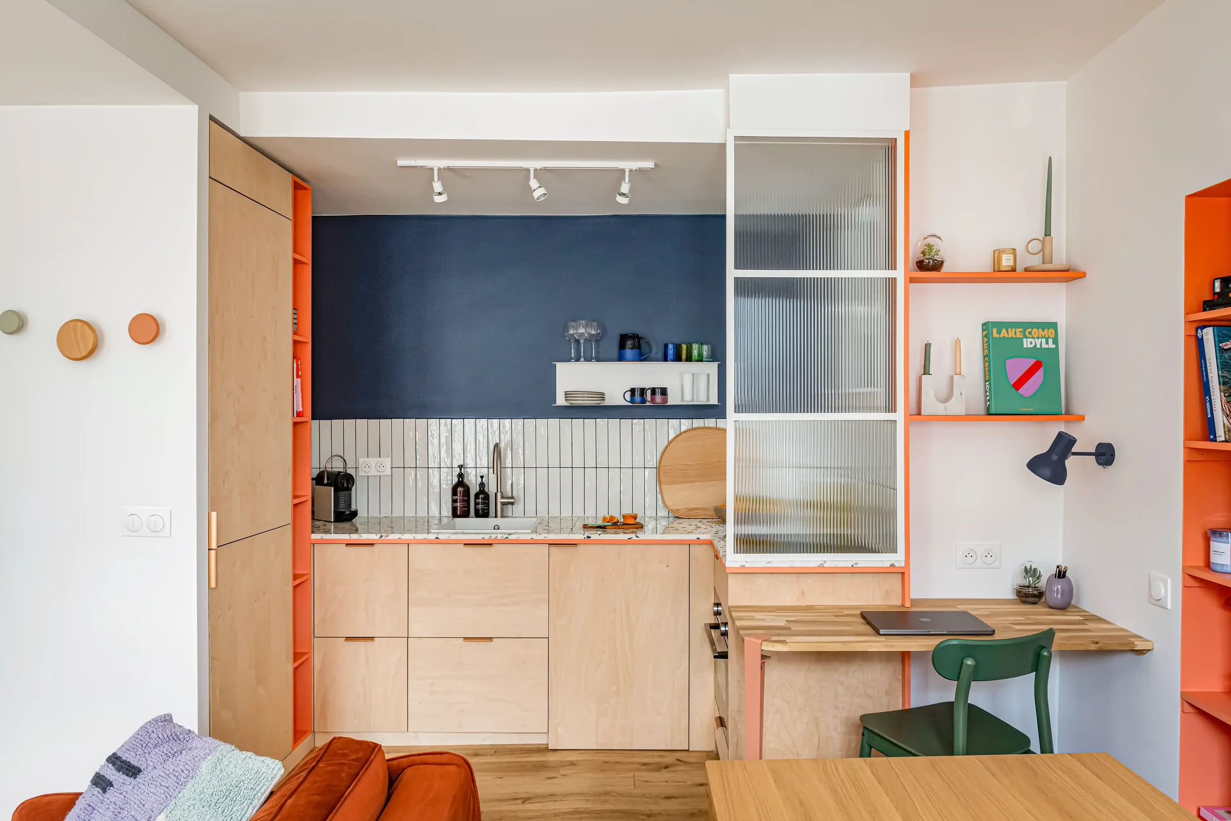 Aménagement de studio coloré avec plan de travail de cuisine en terrazzo et coin bureau intégré.