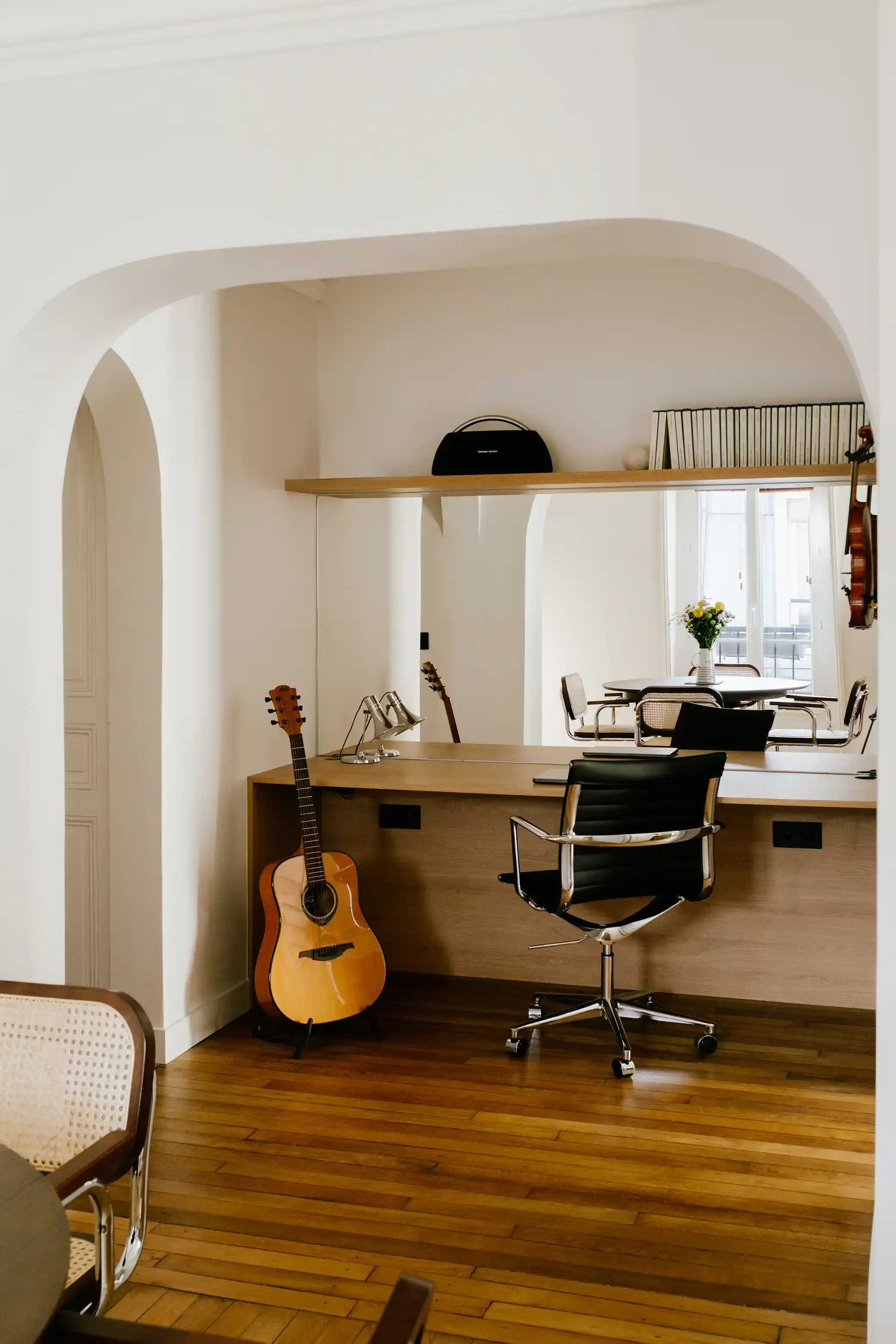 Espace bureau sur-mesure intégré dans une arche avec grand miroir mural, bureau en bois et coin musique avec guitare.