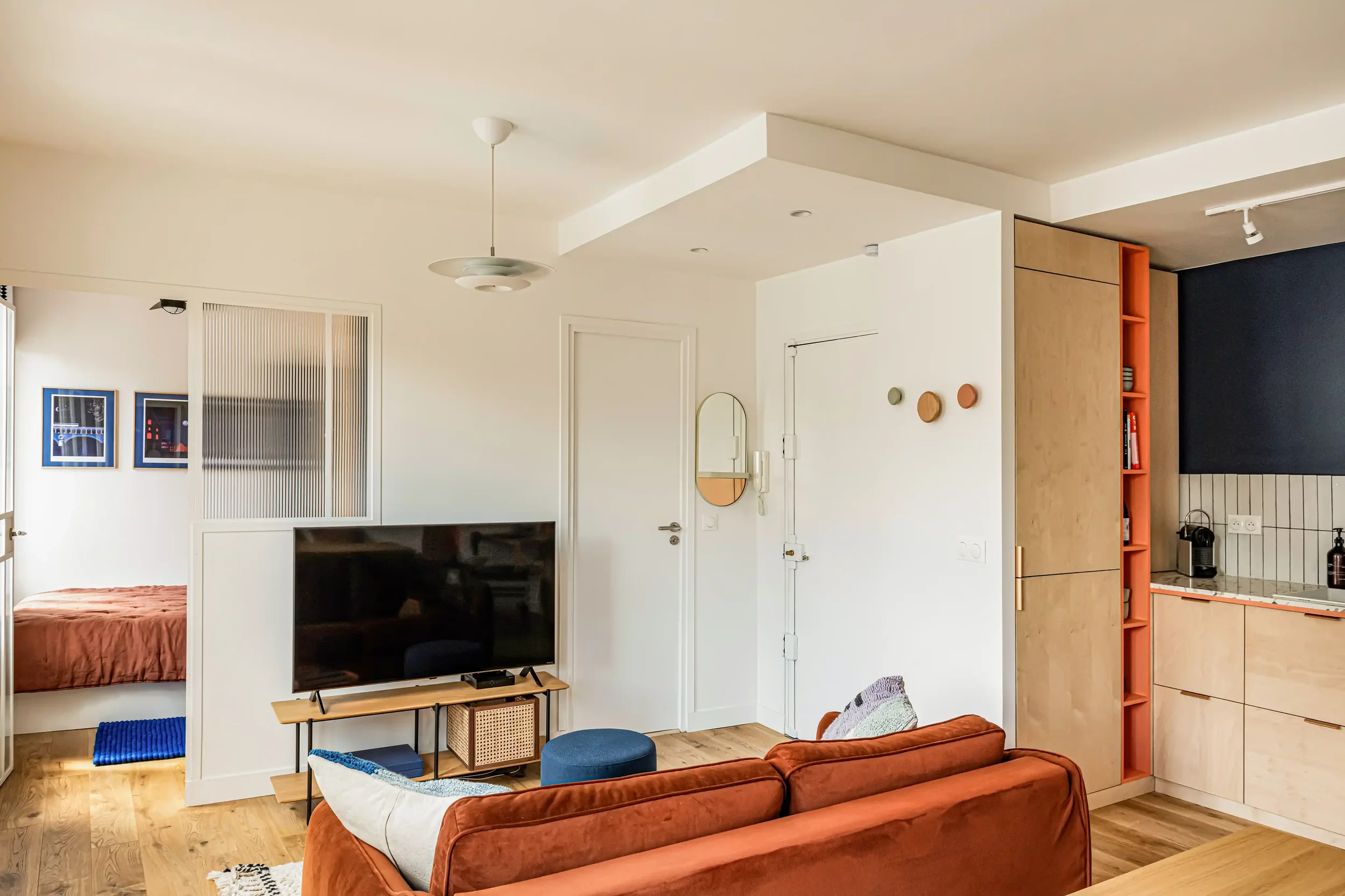 Aménagement d'un petit studio parisien avec canapé terracotta, décoration minimaliste et étagères murales.