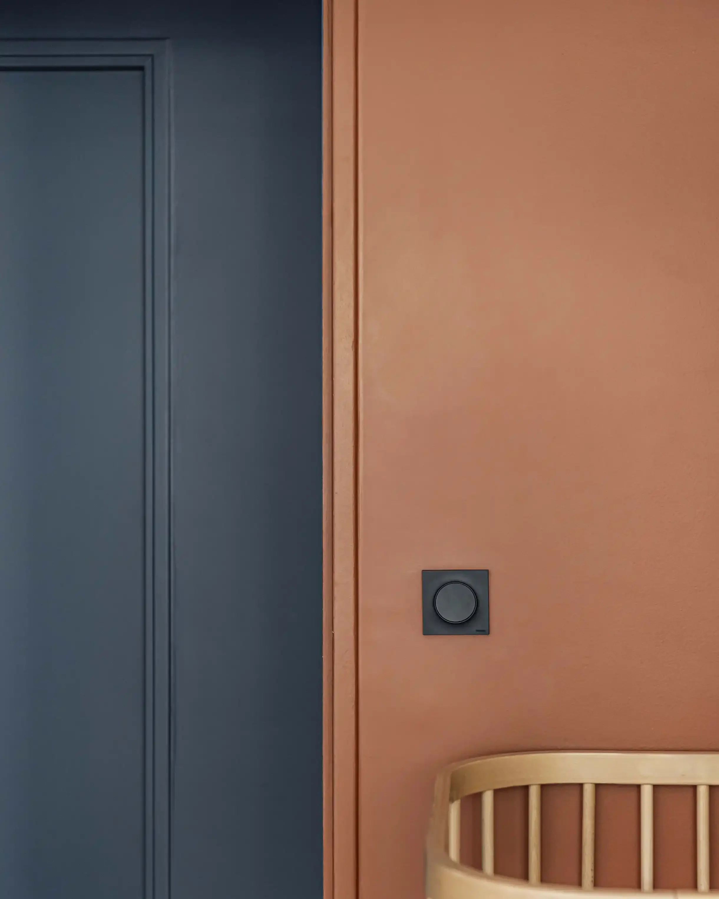 Zoom sur mur peint en terracotta avec interrupteur noir design et étagère en bois dans une chambre d'enfant.