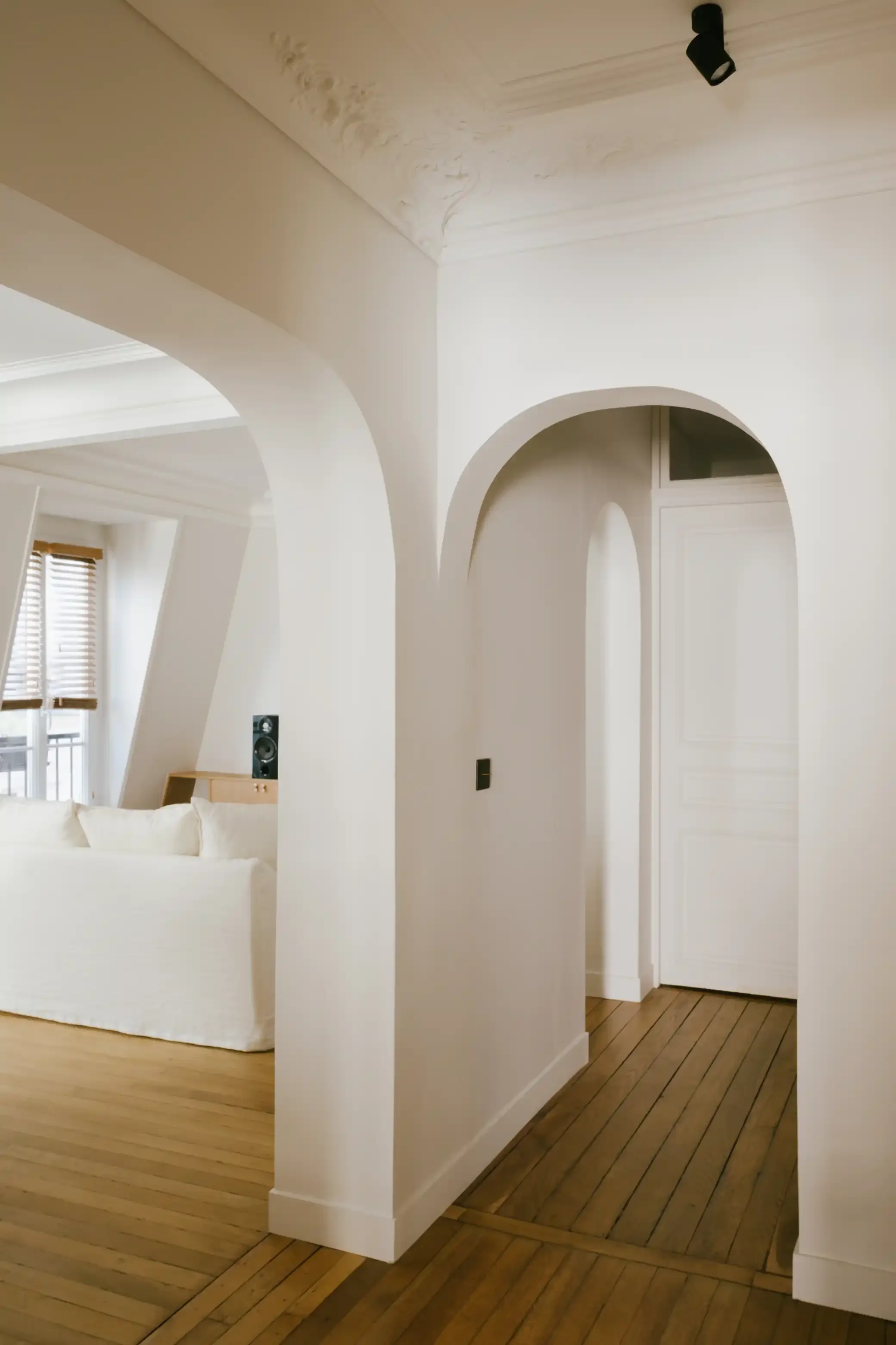 Appartement style bohème chic avec plusieurs arcades blanches structurelles, moulures au plafond et parquet ancien.