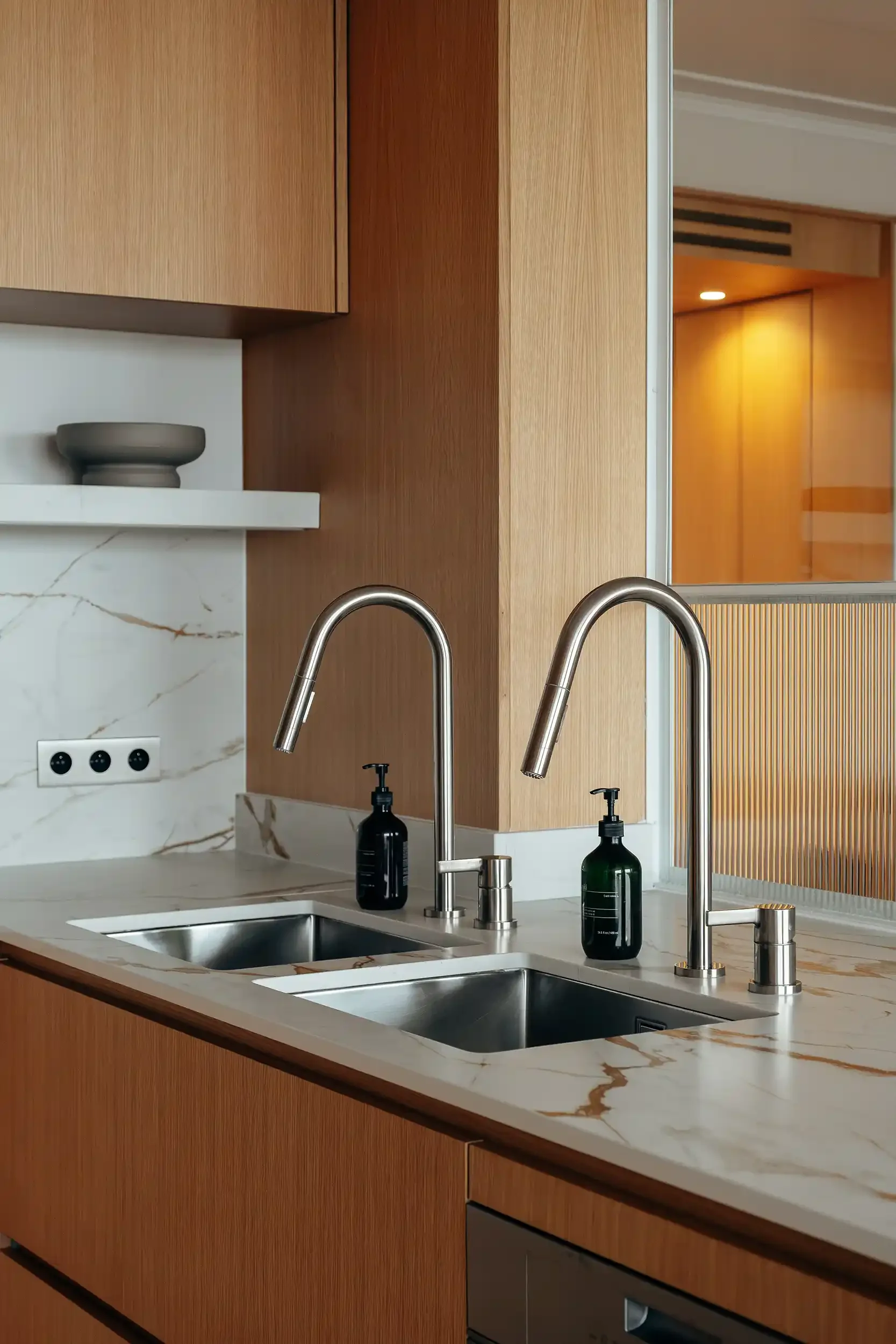 Double robinetterie de cuisine avec douchettes extractibles sur un évier en inox et plan de travail en marbre blanc.