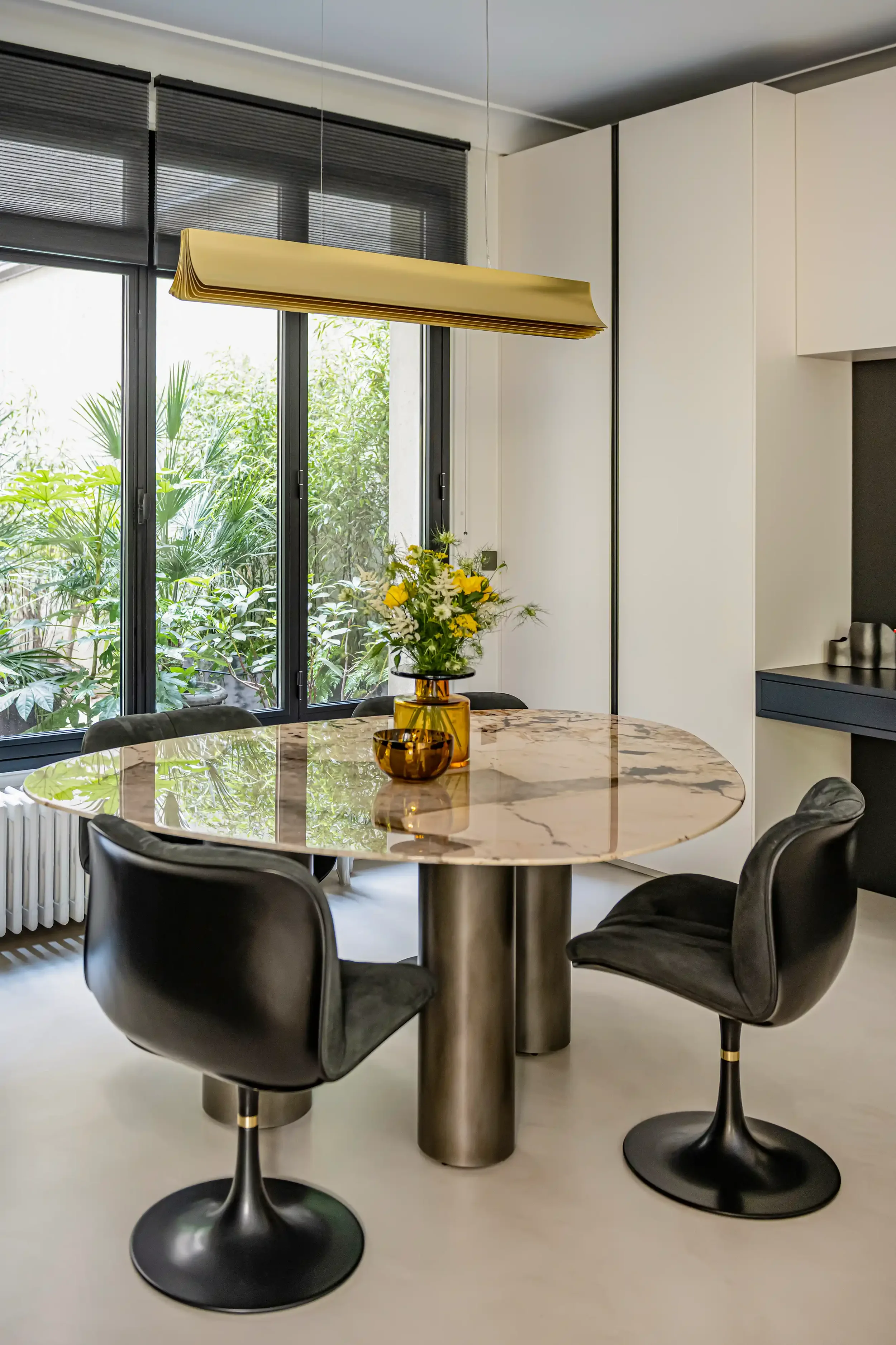 Salle à manger de luxe avec table ronde en marbre veiné, chaises pivotantes noires et suspension design en laiton.