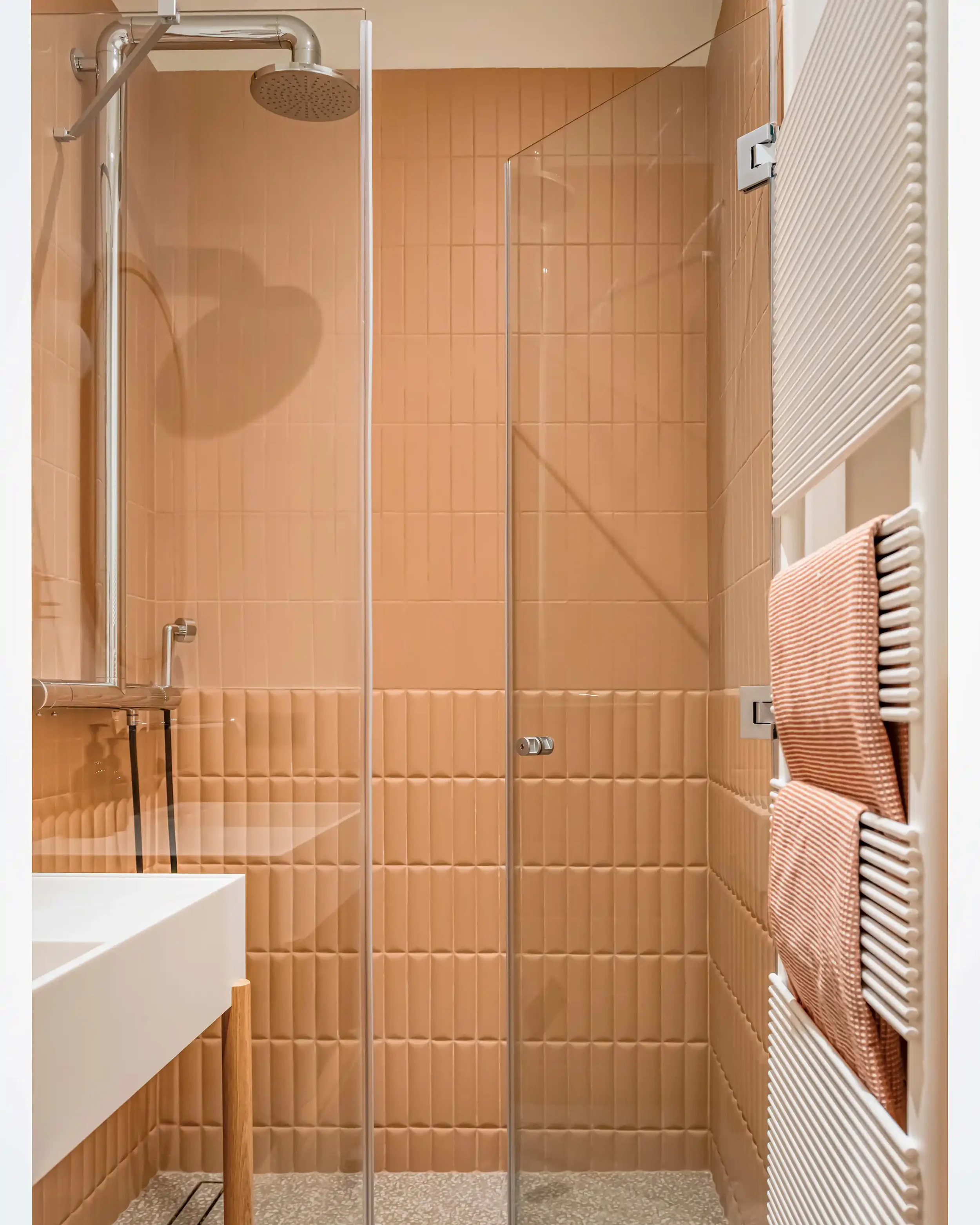 Salle de bain contemporaine avec mur en zelliges orange terracotta, colonne de douche chromée et sèche serviette design.
