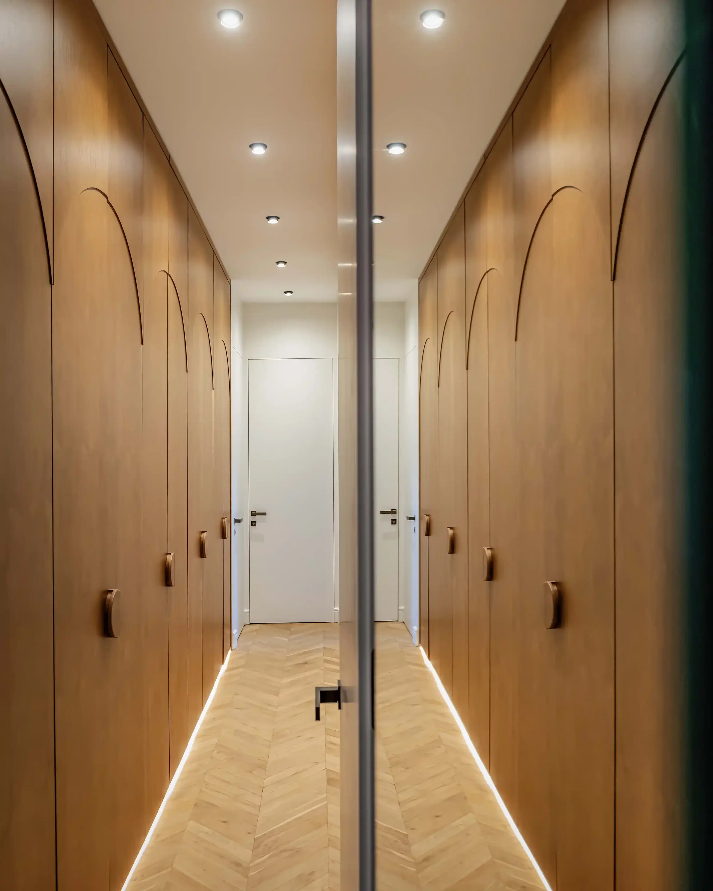 Couloir étroit optimisé avec des rangements toute hauteur en bois chaleureux, éclairage LED au sol et parquet en point de Hongrie.