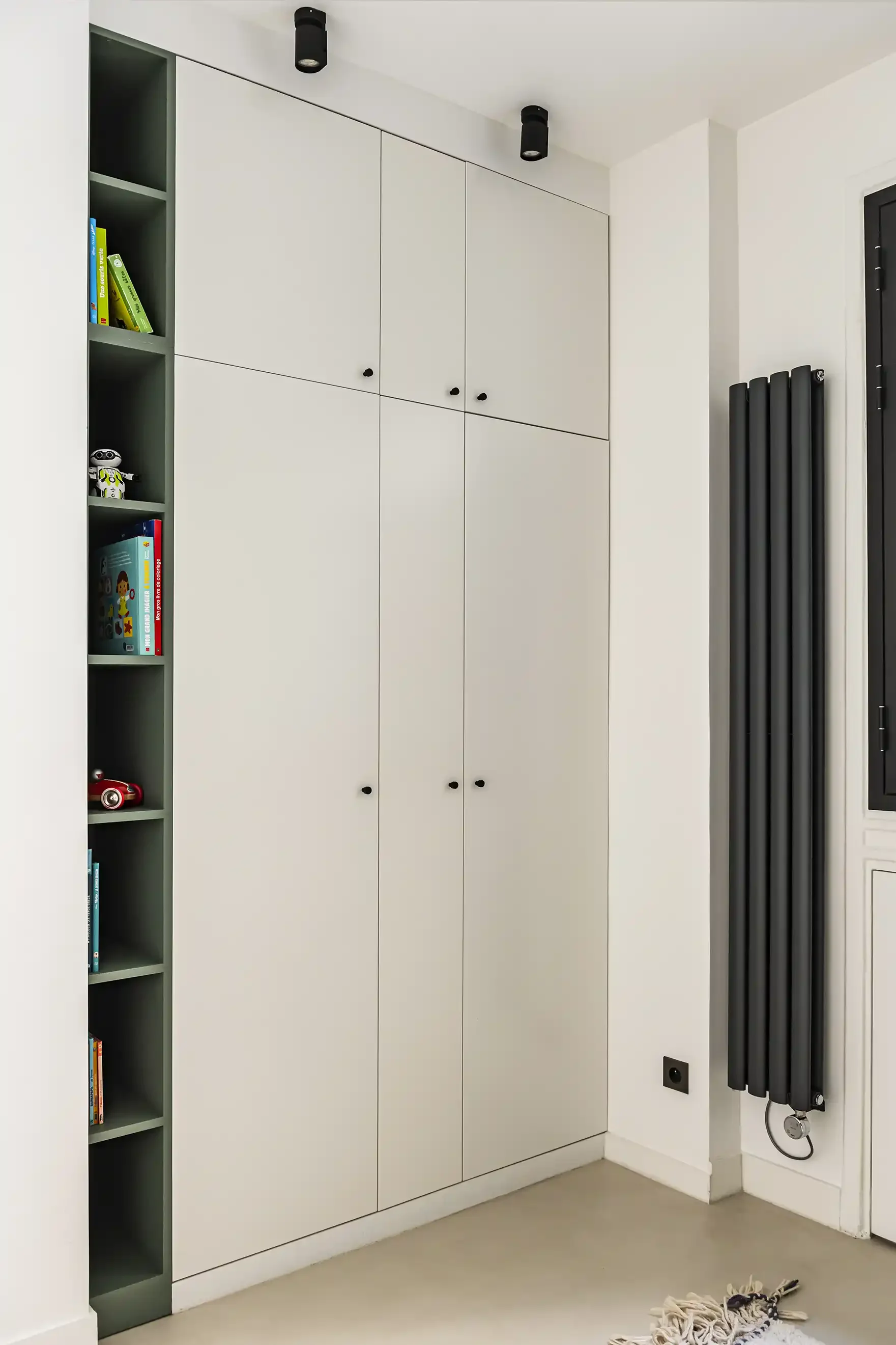 Grand placard de rangement sur mesure blanc avec une fine colonne bibliothèque intégrée de couleur vert sauge et radiateur vertical noir.