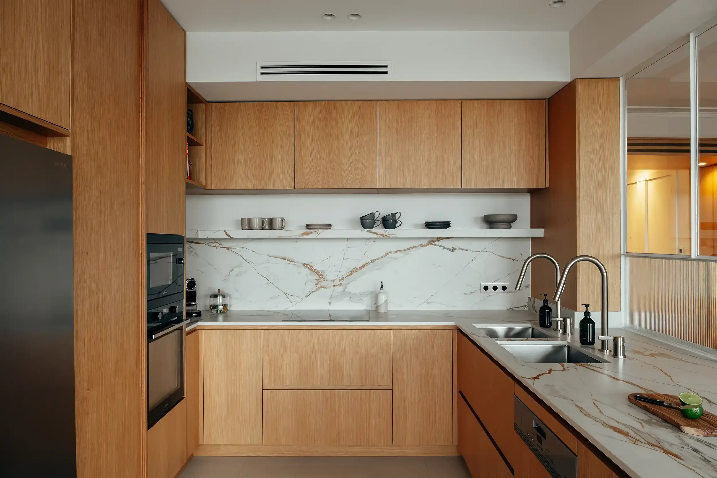 Cuisine en U moderne avec façades en chêne clair, plan de travail en marbre blanc veiné d'or et crédence assortie.