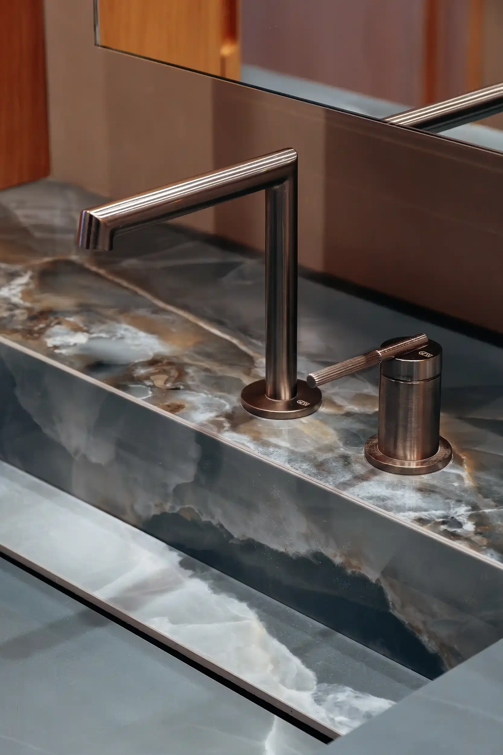 Mitigeur de lavabo design en finition bronze brossé installé sur un plan de travail en onyx bleu nervuré.