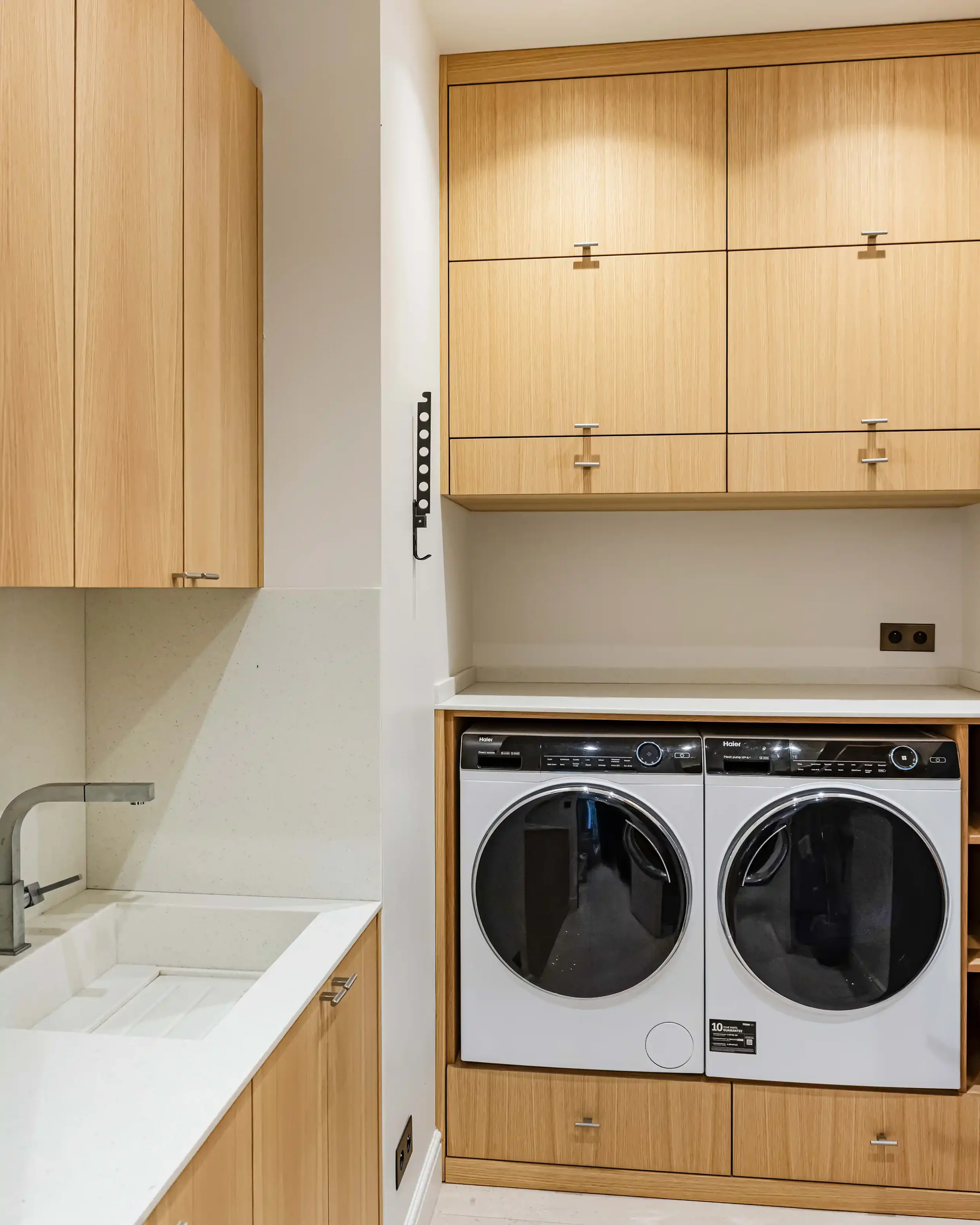 Aménagement d'une buanderie sur mesure en bois de chêne clair avec rangements intégrés dans un appartement parisien.
