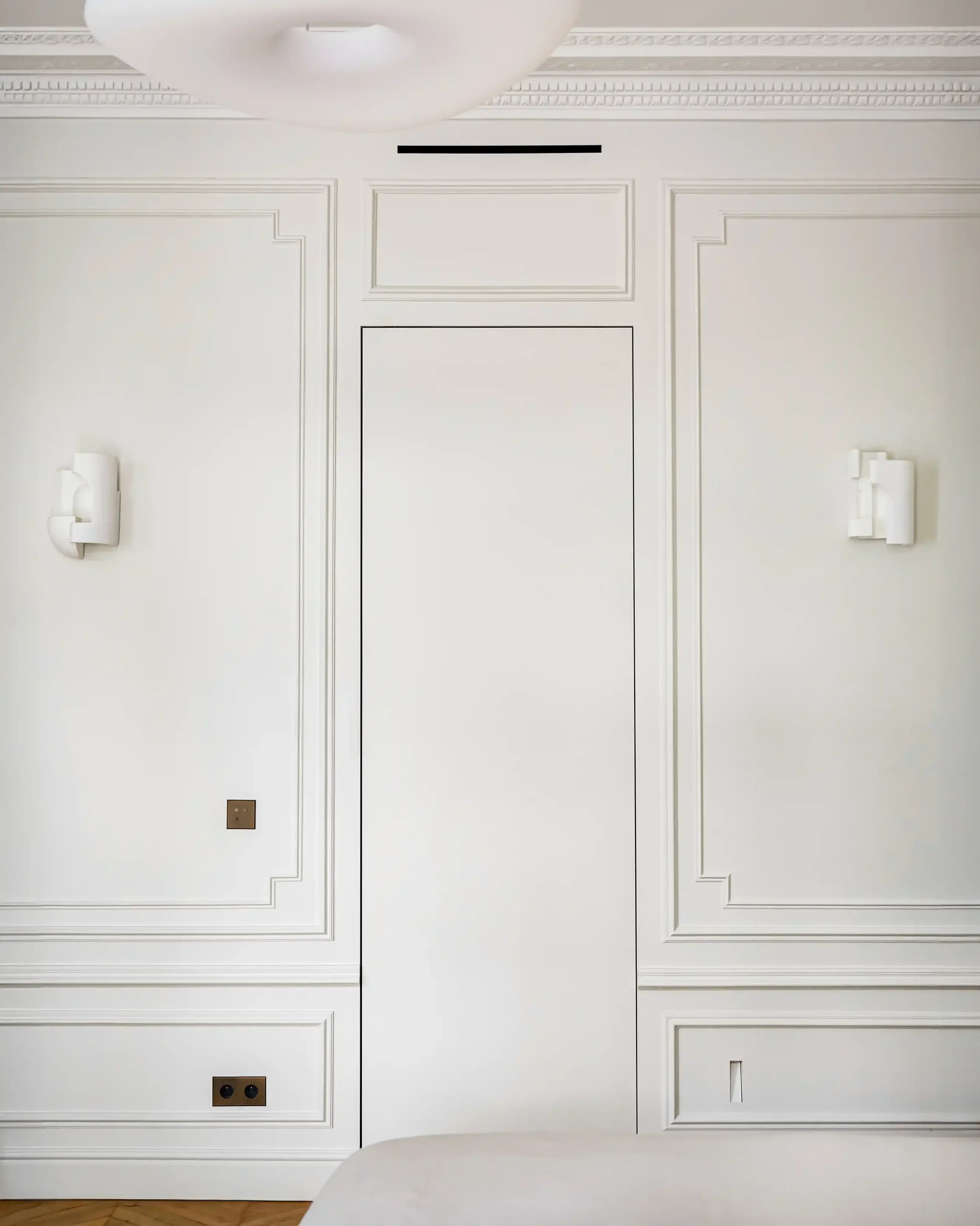 Détail de moulures murales classiques blanches intégrant une porte invisible sous tenture pour un effet minimaliste.