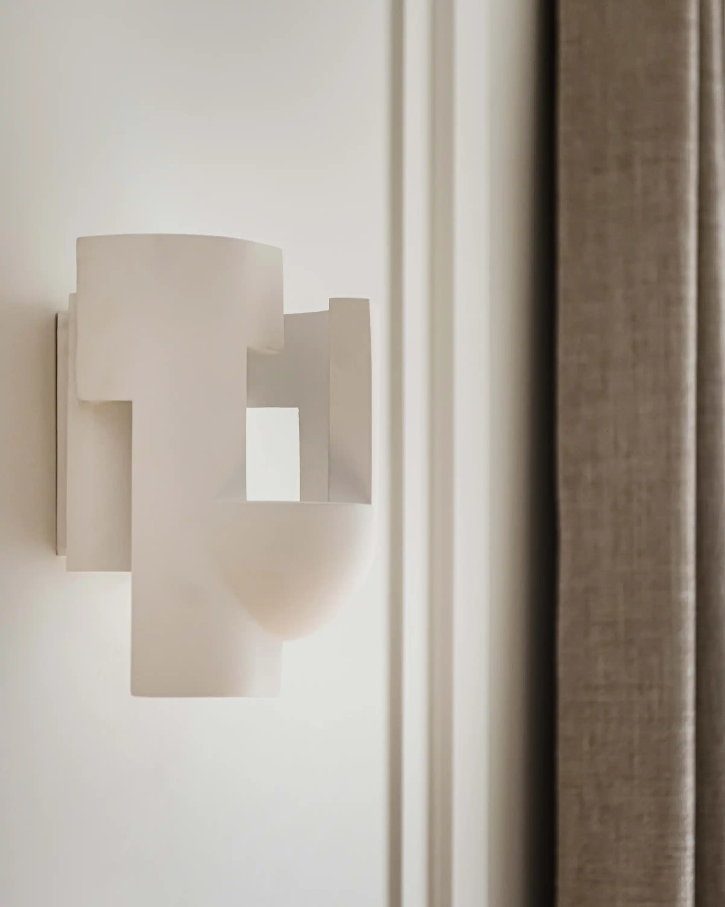 Zoom sur une applique murale design sculpturale blanche installée sur un mur à moulures élégantes.