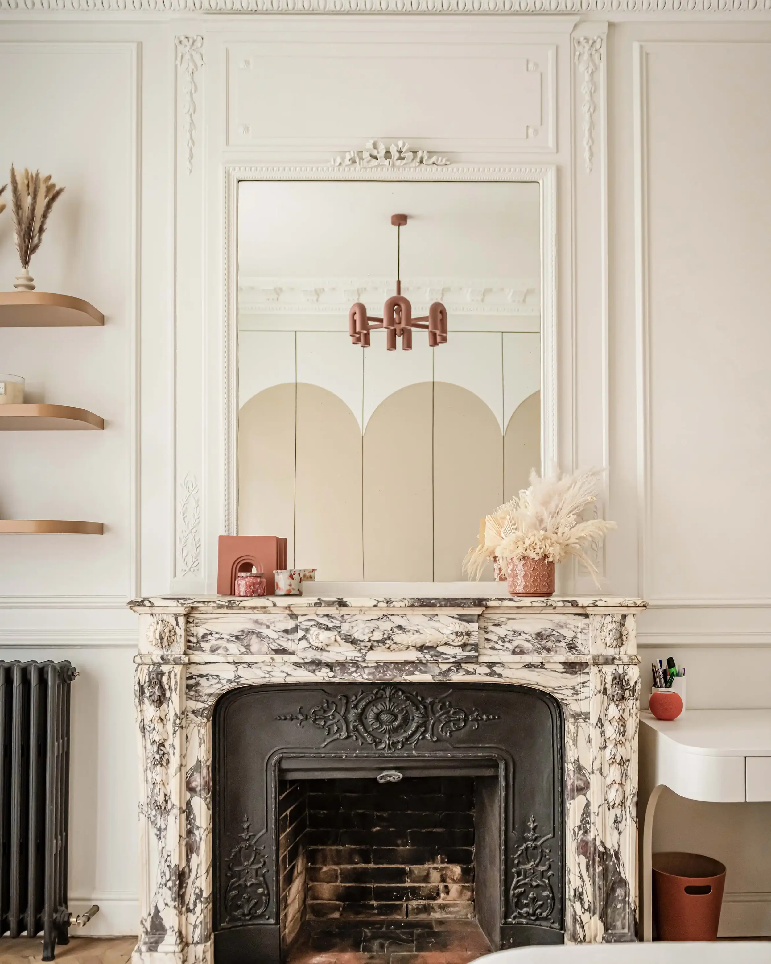 Cheminée ancienne en marbre veiné noir et blanc avec foyer en fonte sculpté et grand miroir trumeau intégré.