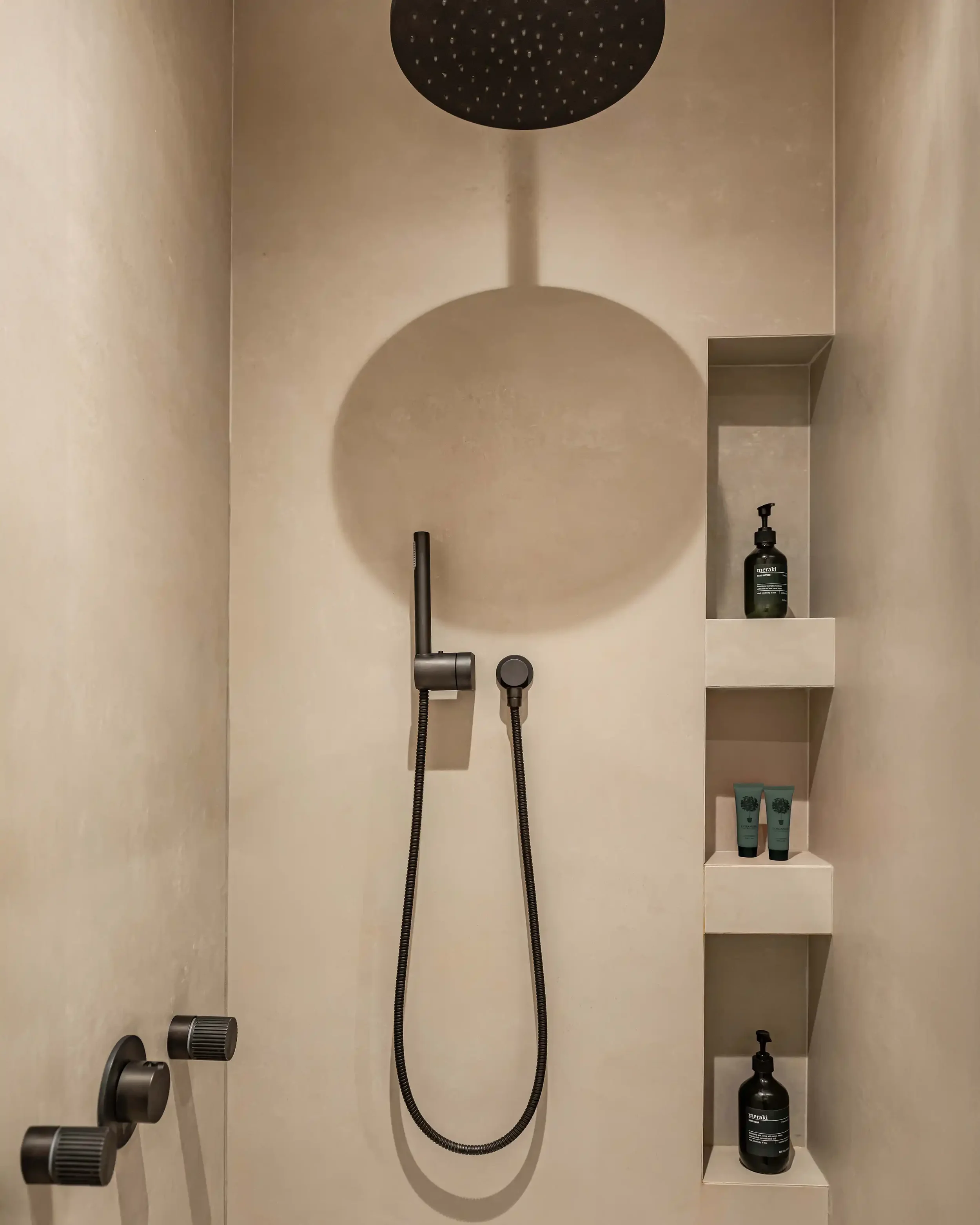 Détail d'une douche à l'italienne en pierre naturelle grège avec niches de rangement intégrées et robinetterie encastrée noire mate.