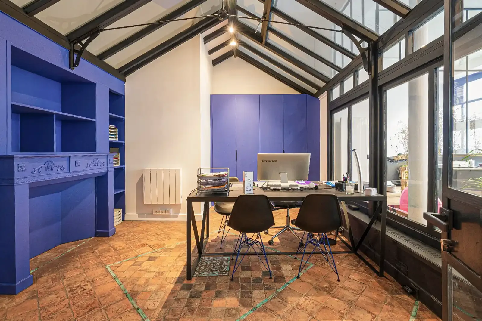 Vue de profil d'un bureau de direction lumineux avec verrière de toit, bibliothèque bleue sur mesure et fauteuils design.