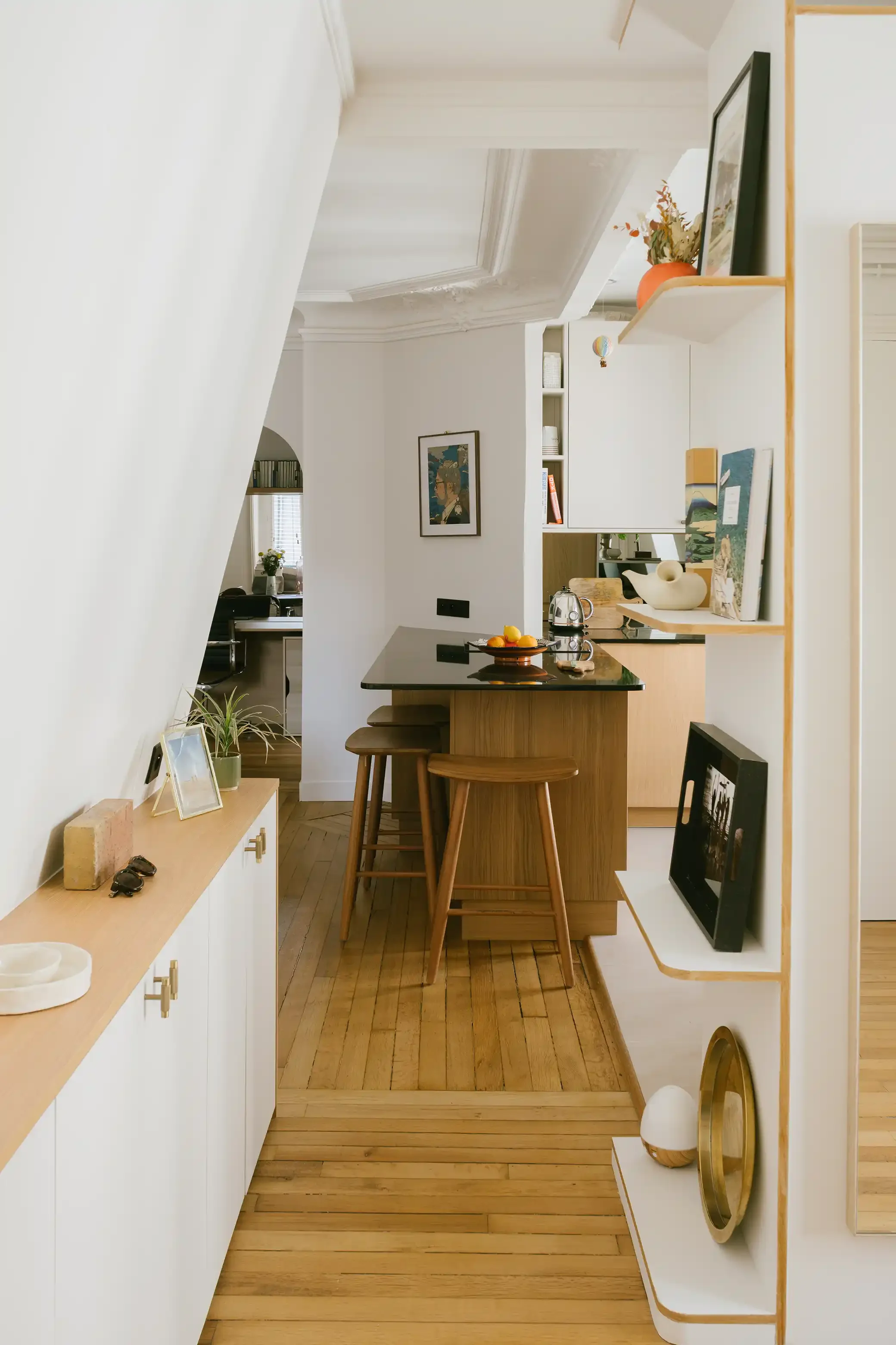 Cuisine ouverte avec îlot central en bois, plan de travail noir et tabourets design dans un appartement rénové du 10ème arrondissement de Paris.