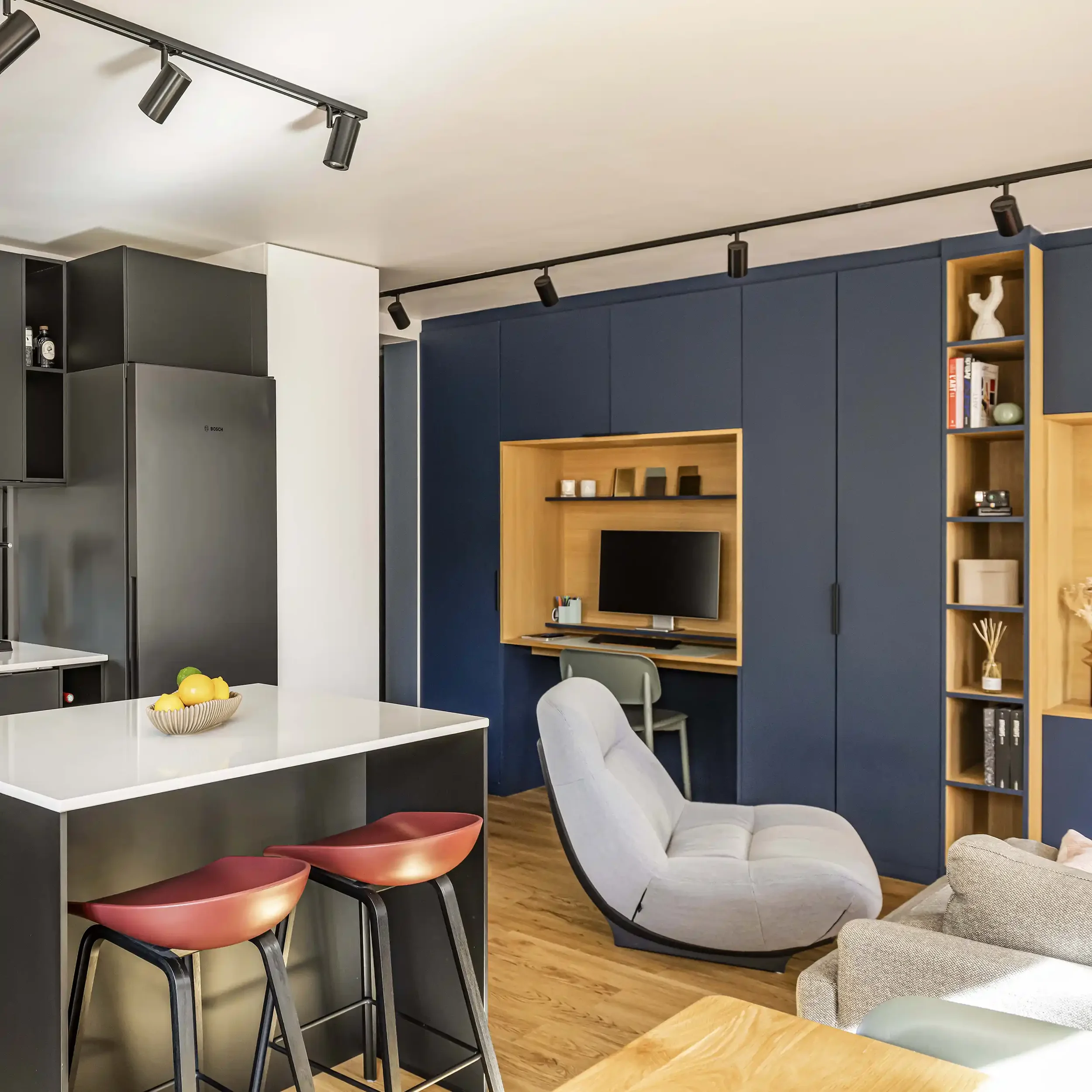 Espace de vie ouvert avec bureau intégré sur mesure dans un grand meuble de rangement bleu foncé.