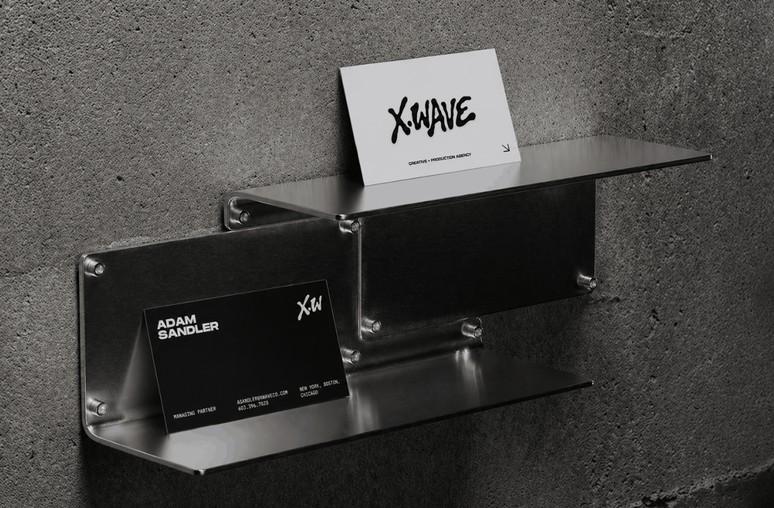 Black and white business card designs displayed on brushed metal shelves, showcasing custom typography and branded stationery for a creative agency identity system.