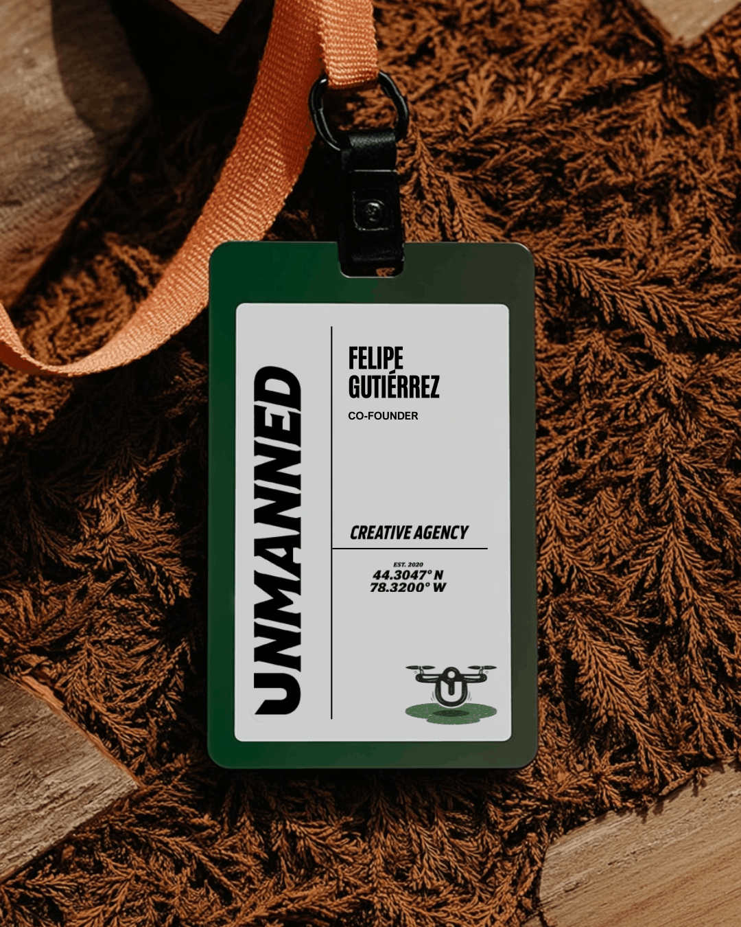 Branded employee name badge with custom typography and an orange lanyard displayed on textured foliage, showcasing identity design for a creative marketing agency.