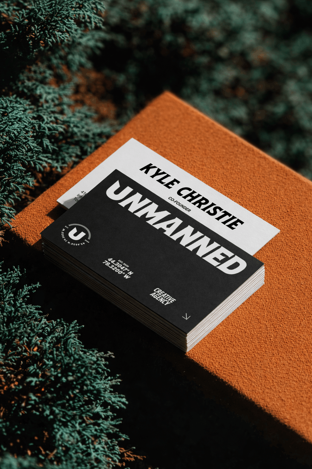Black and white business cards featuring bold typography displayed on an orange tabletop, showcasing branded stationery for a creative marketing agency.