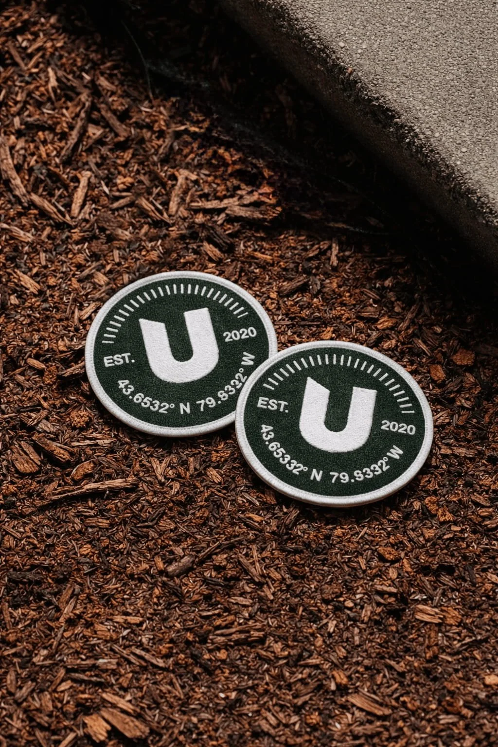Embroidered brand patches featuring a custom logo displayed on natural wood chips as part of a creative marketing agency merchandise collection.