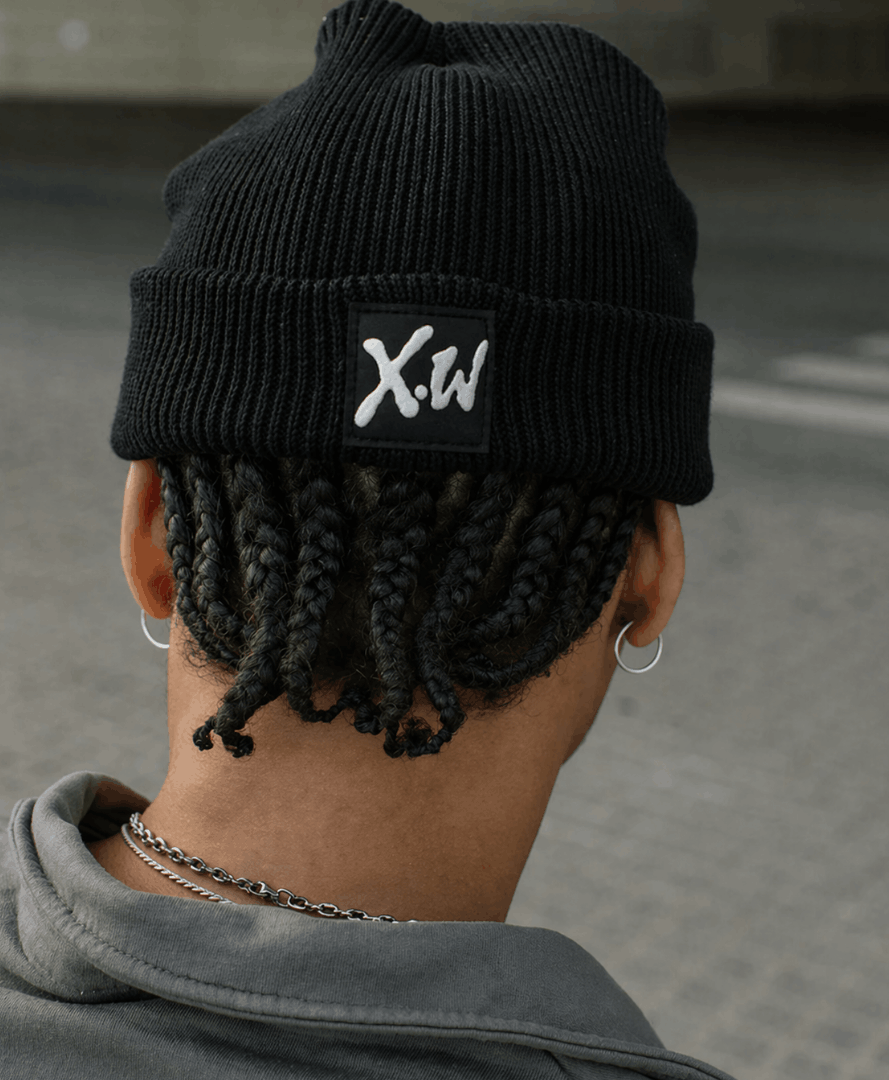 Rear view of a person wearing a black knit beanie with a woven logo patch, showcasing branded apparel designed as part of a creative agency identity system.
