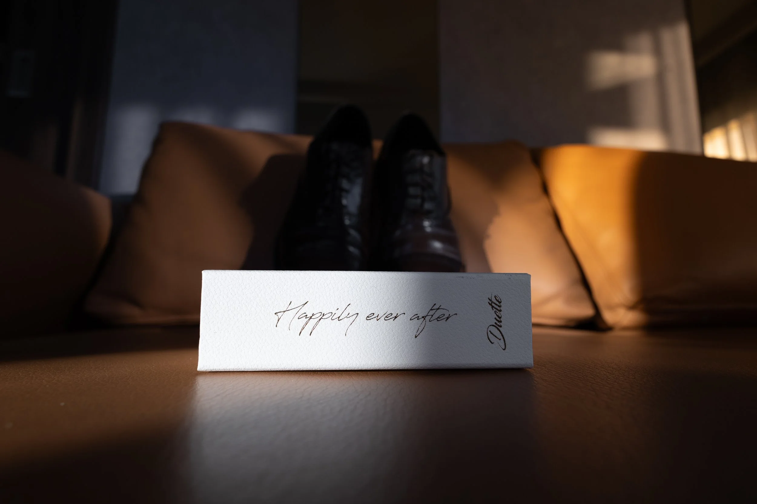 A box with the words "Happily ever after" written on it, sitting on a table with shoes and cushions in the background.