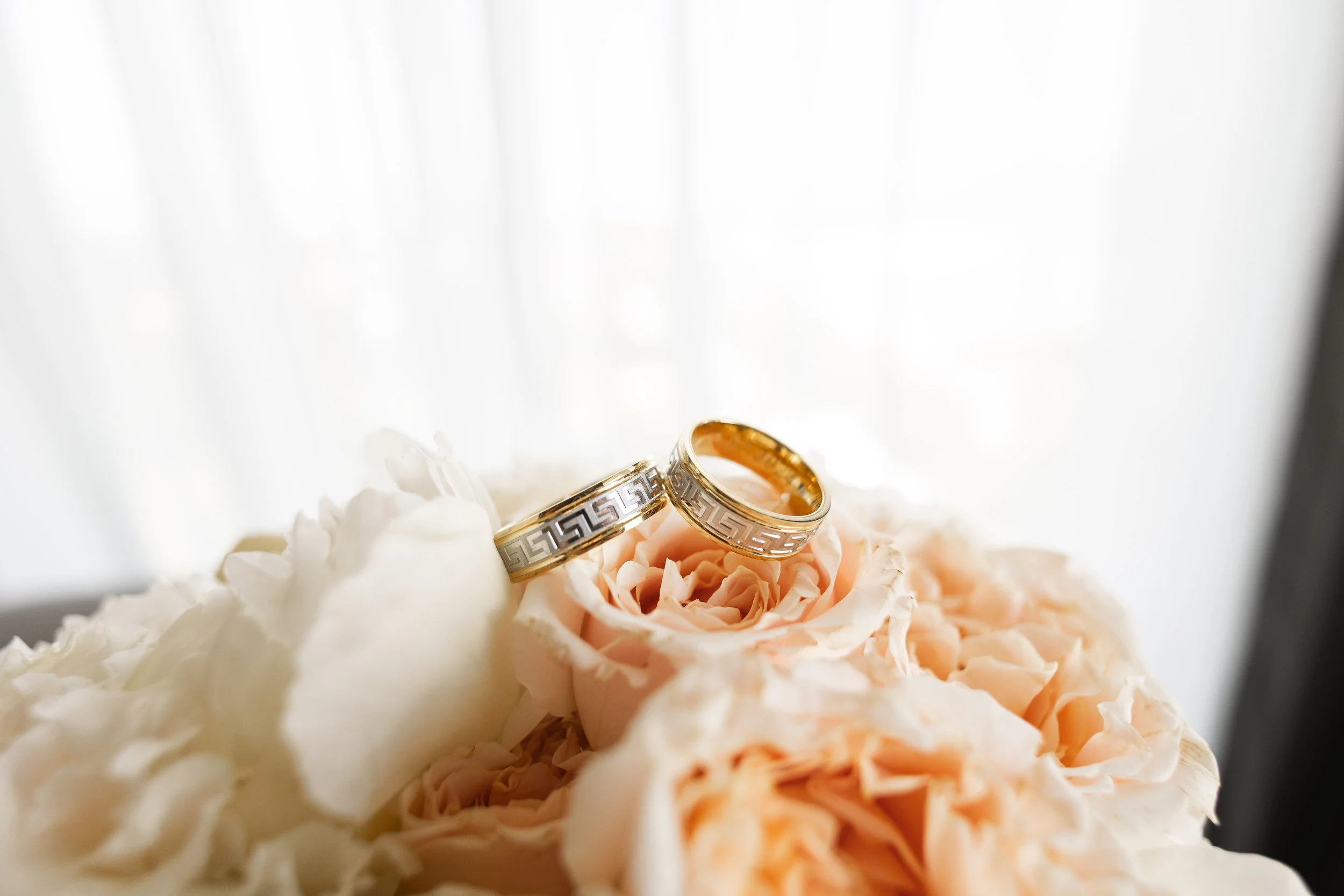 Two wedding rings with Greek key pattern resting on a pink and white peony flower.