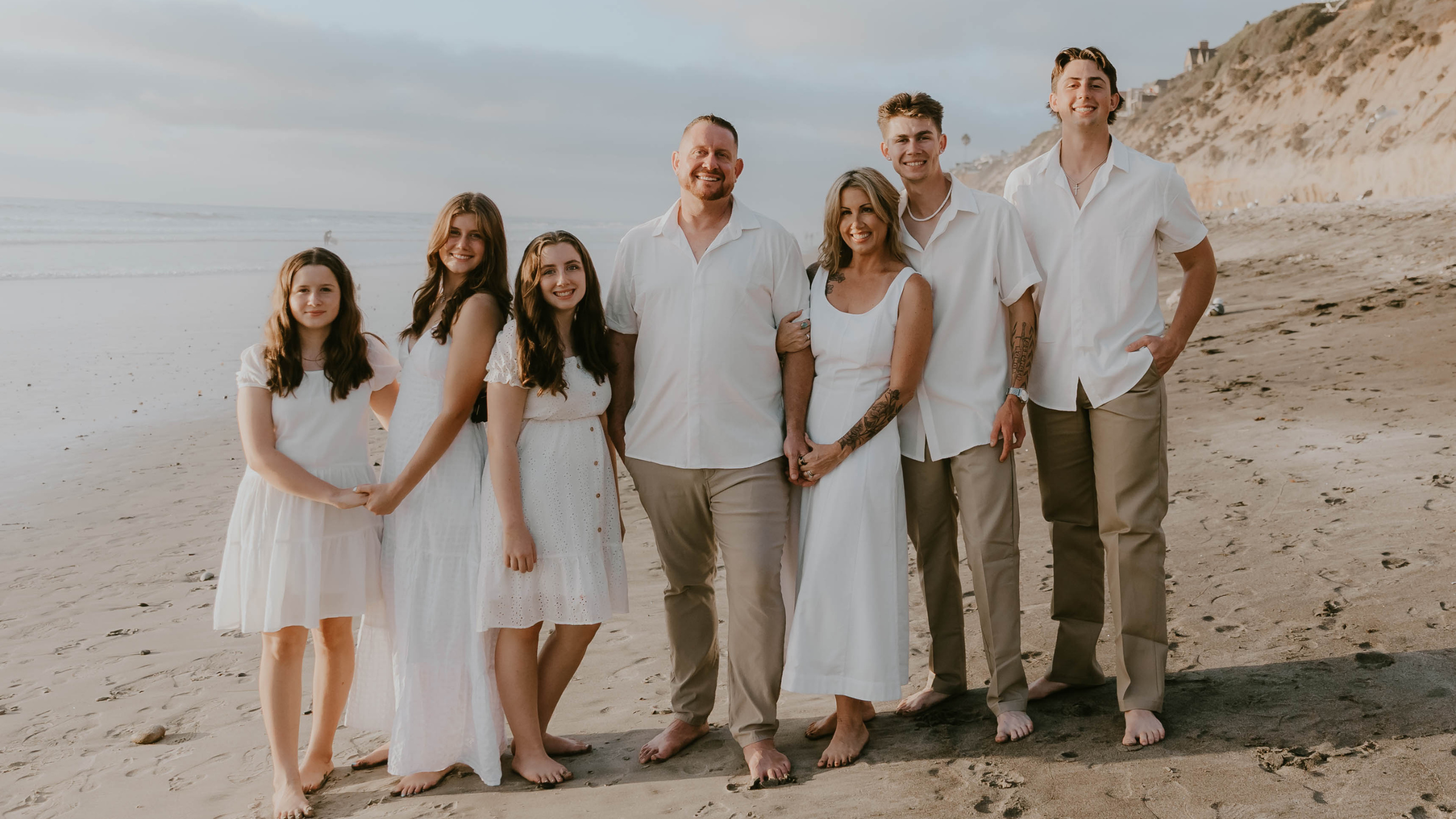 family of husband, wife, and five kids standing on beach in front of ocean in white shirts, owners of Universal Modular, Inc.