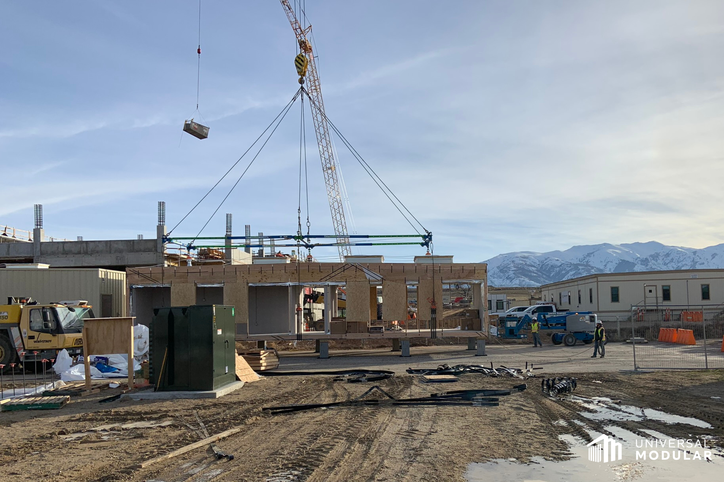 outdoor image of modular construction site with partially built building, crane lifting materials, and mountains in the background