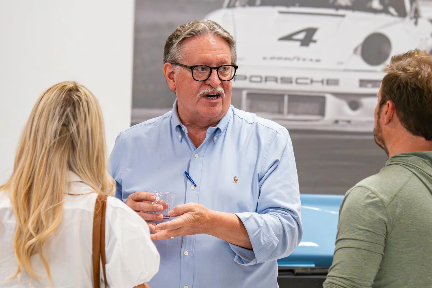 Networking conversation at an automotive gallery with Porsche backdrop — corporate reception photography.