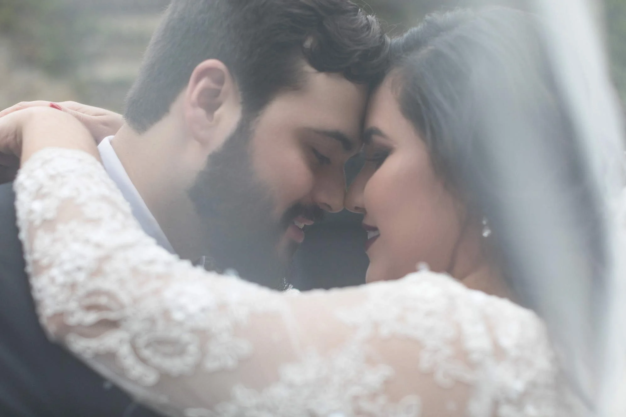 A close-up of a bride and groom with foreheads touching and eyes closed, smiling, during their wedding.