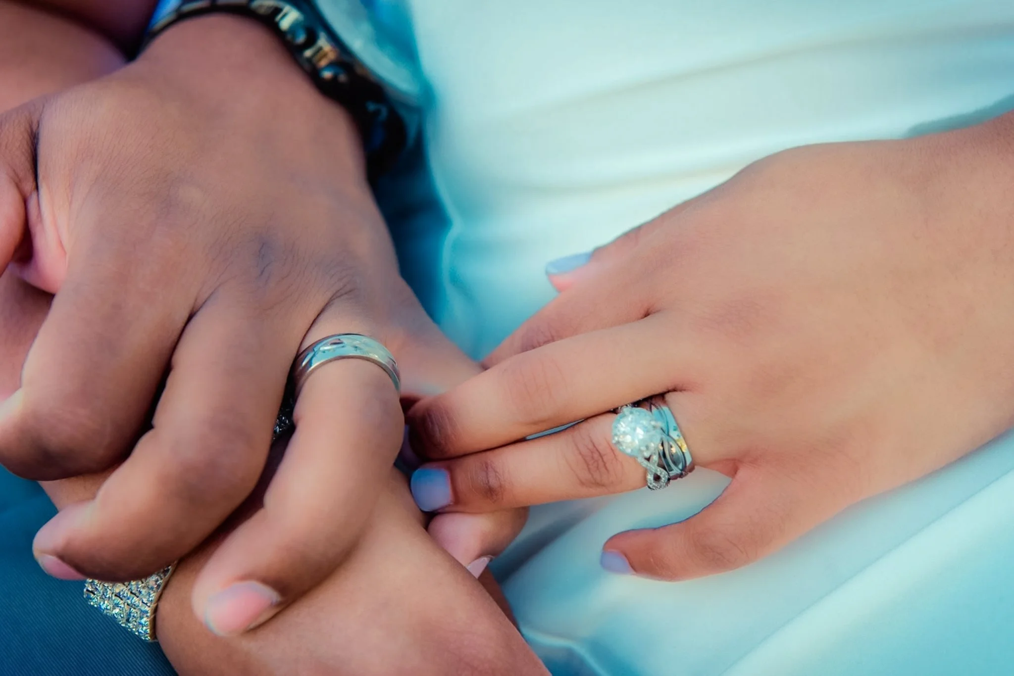 Close-up of multiple hands with various rings overlapping each other, resting on a light teal fabric surface.