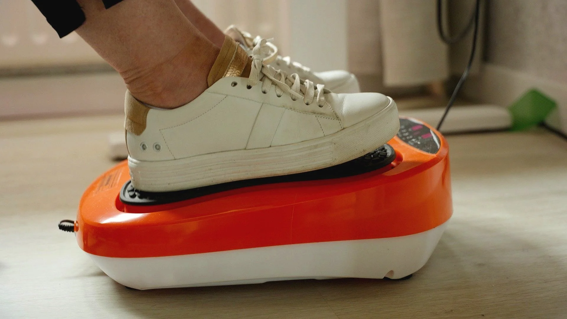 Voet met witte sneaker op een oranje fitnessapparaat.