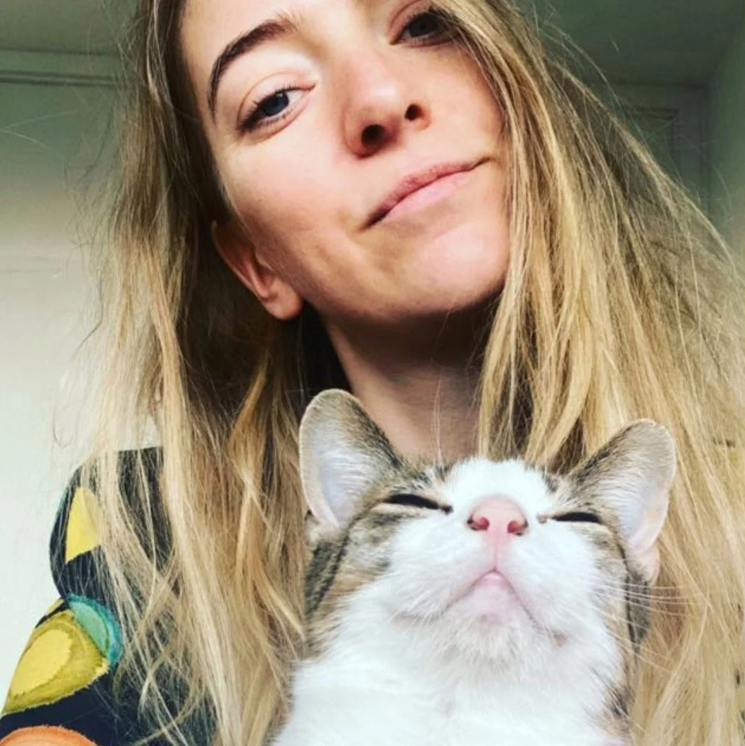 Vrouw met lang blond haar glimlacht zachtjes naast een tevreden uitziende kat.