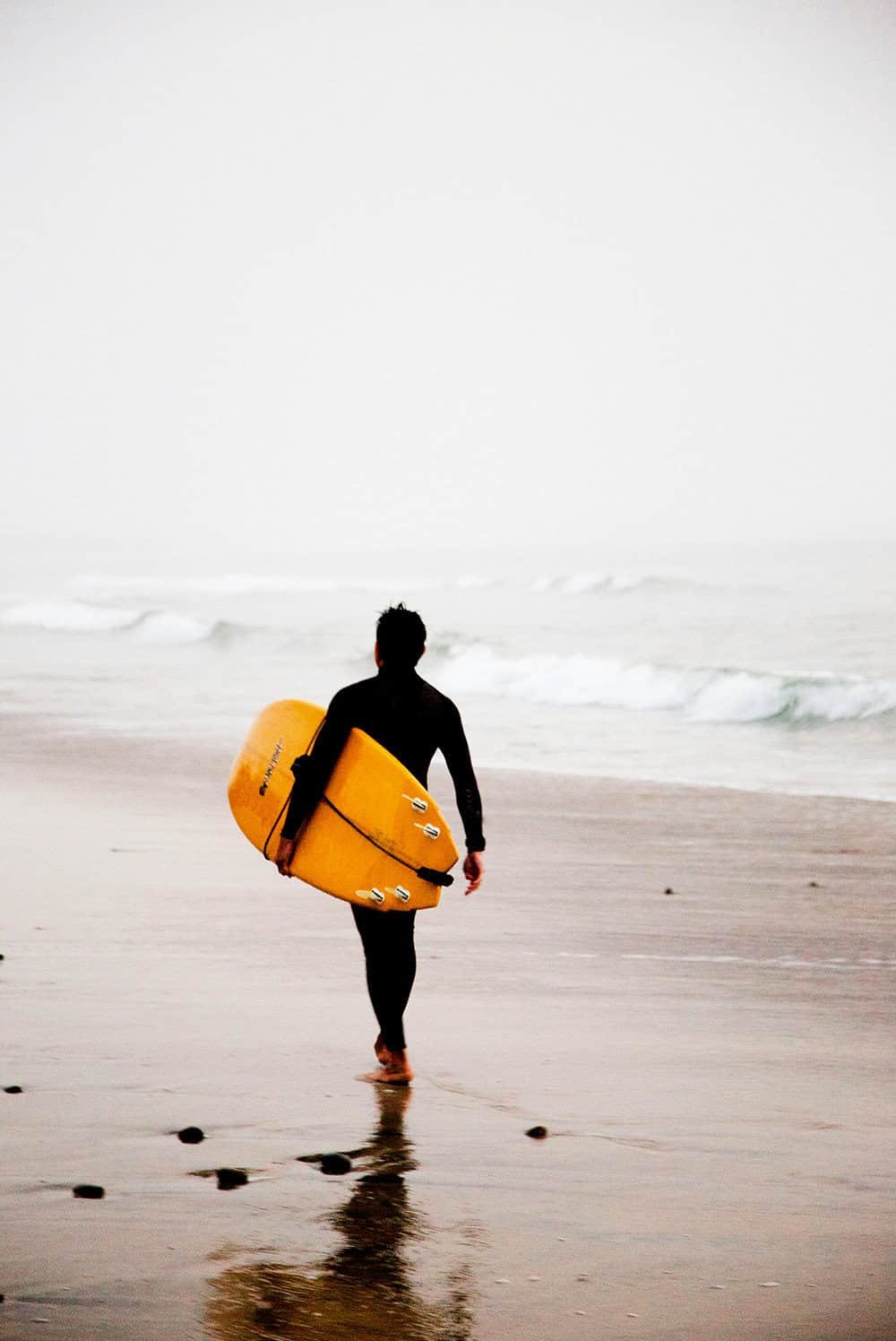 A print of a lone surfer, poised with a vibrant yellow surfboard, heading towards the misty ocean waves.