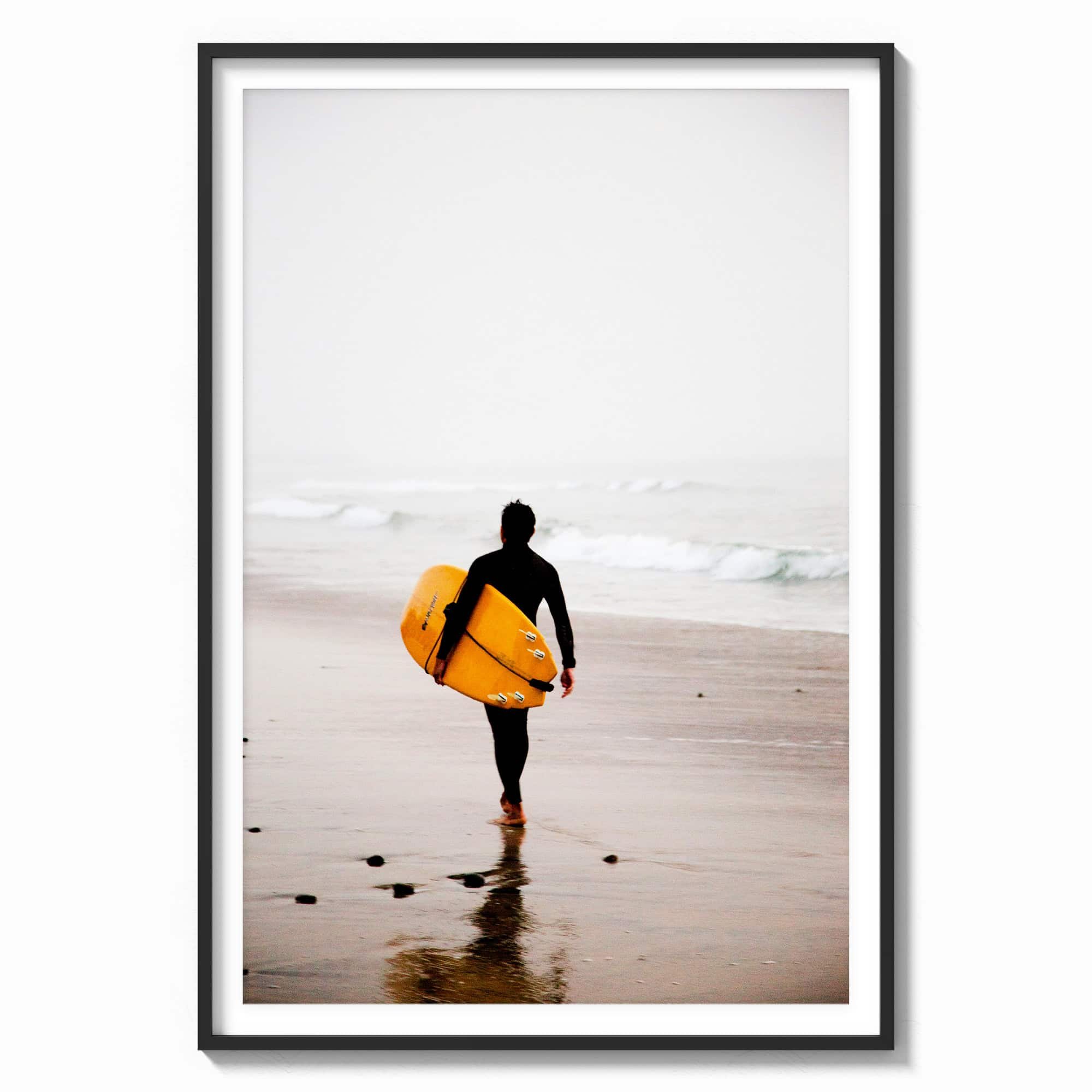 This stunning wall art features a lone surfer, poised with a vibrant yellow surfboard, heading towards the misty ocean waves in a black wood frame.