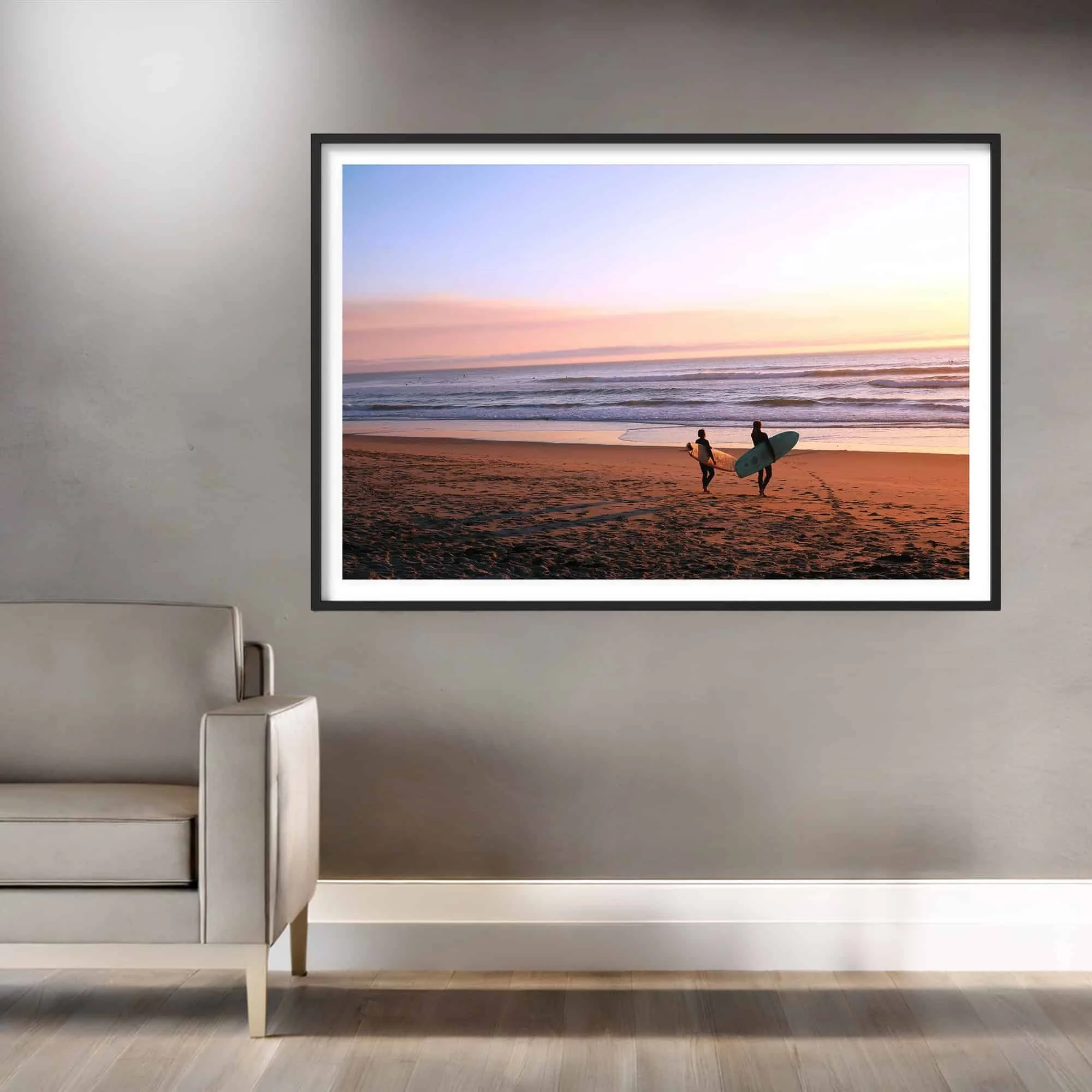 two surfers on the beach at sunset with pink, blue and yellow sky print with black wood frame in living room