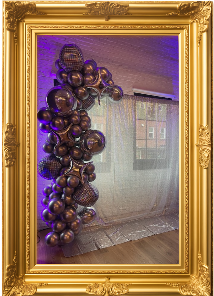 A cluster of metallic balloons in various sizes including some with a disco mirror pattern, arranged along a wall with purple lighting and a sheer curtain in the background.