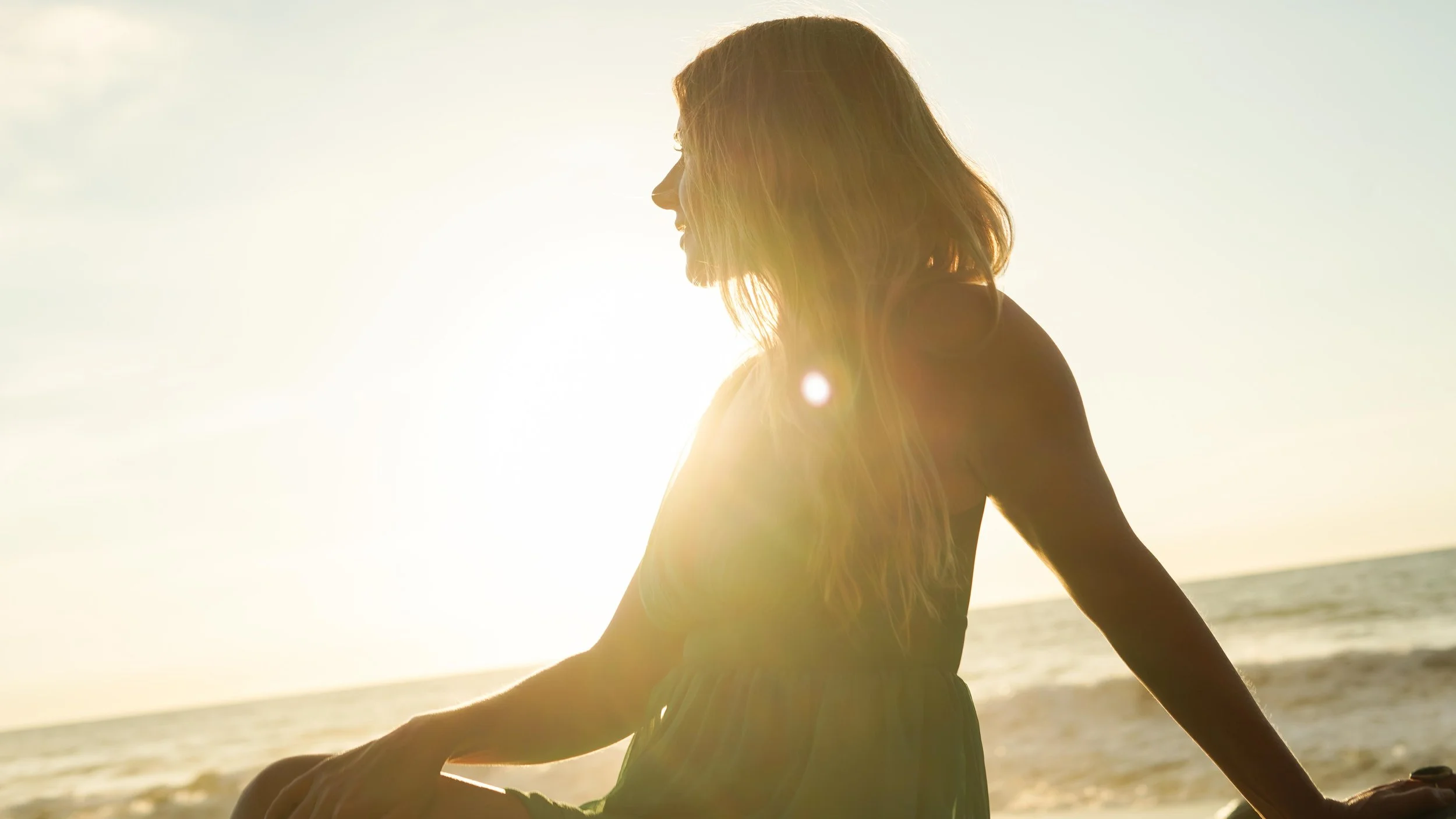 Person with long hair sitting on the beach during sunset