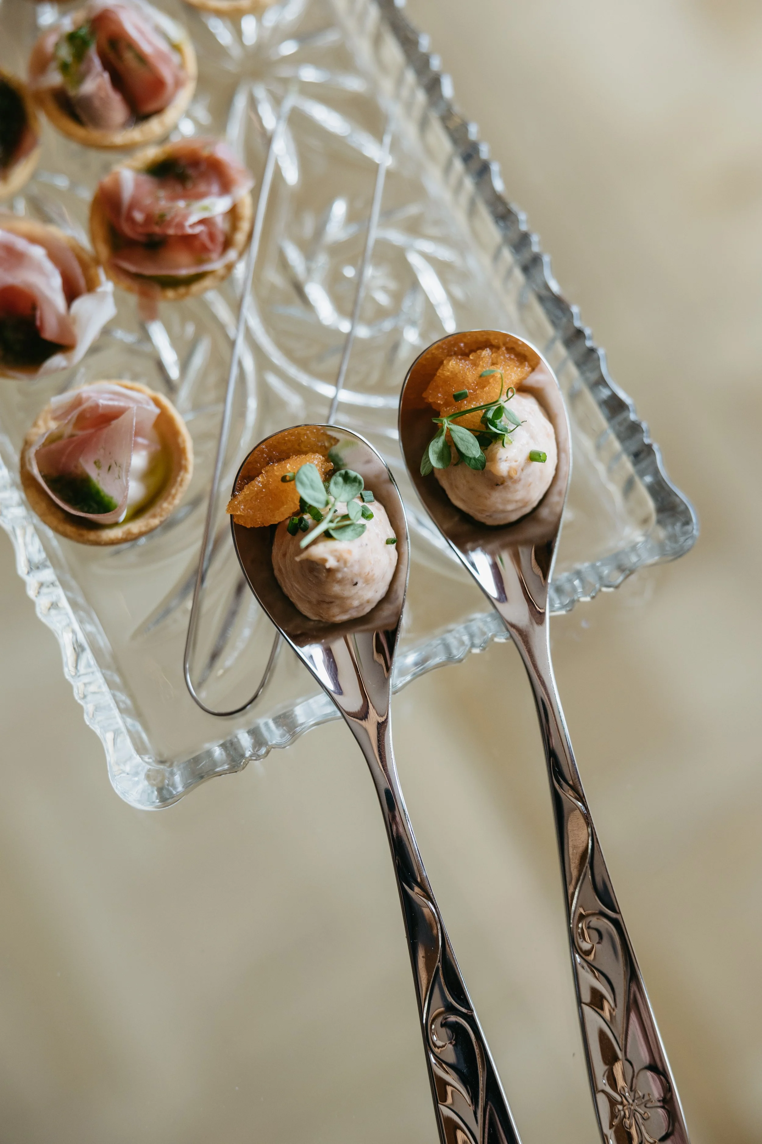 To asiatiske forrettter med mousse, garnityr og urter på bestikk, plassert på et glassfat.