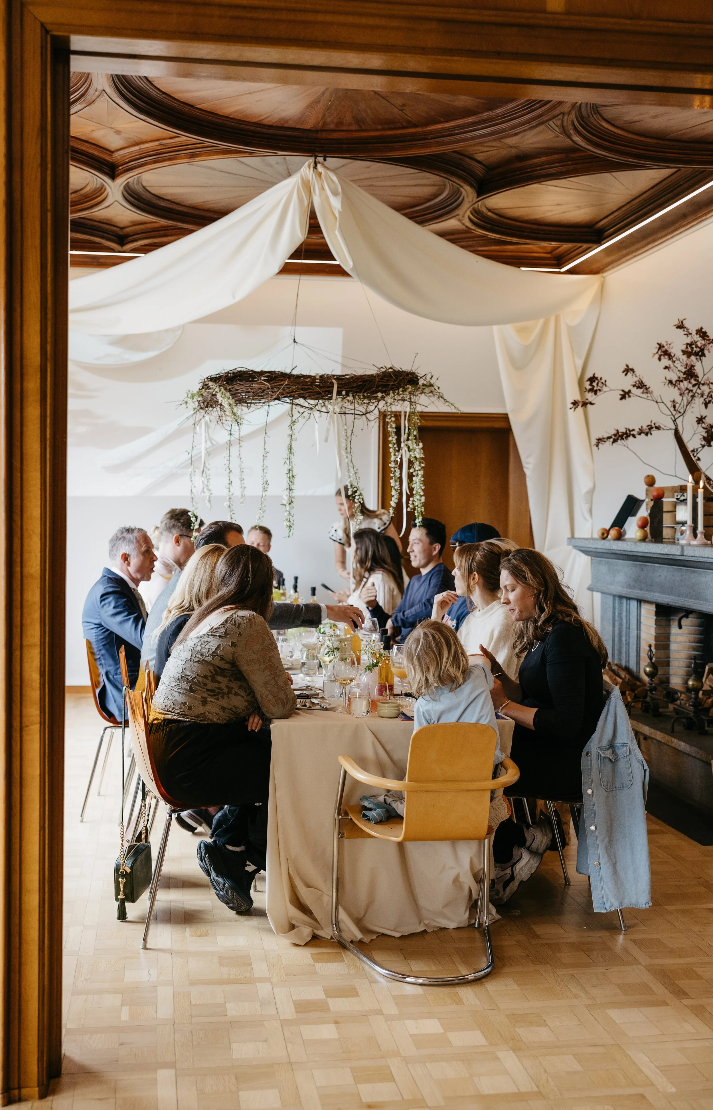 Gjestefest med folk som sitter ved langbord, dekorasjon i taket og peis i rommet.